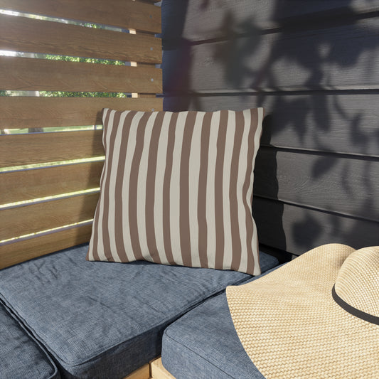 Mocha brown striped outdoor pillow on a blue cushioned outdoor bench with a straw hat nearby.