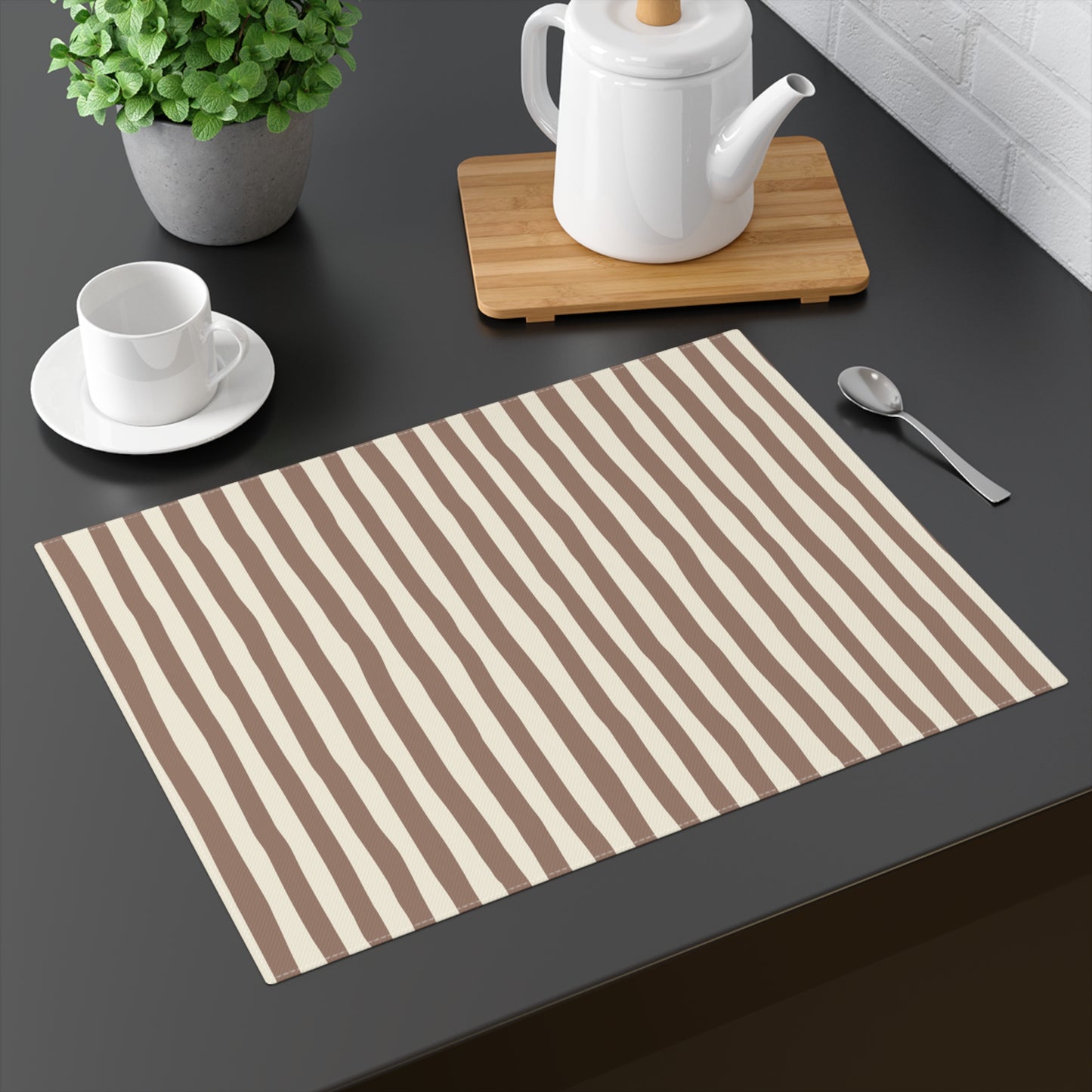 Mocha Striped placemat with brown and beige stripes on a dark surface with a teapot, cup, and spoon.
