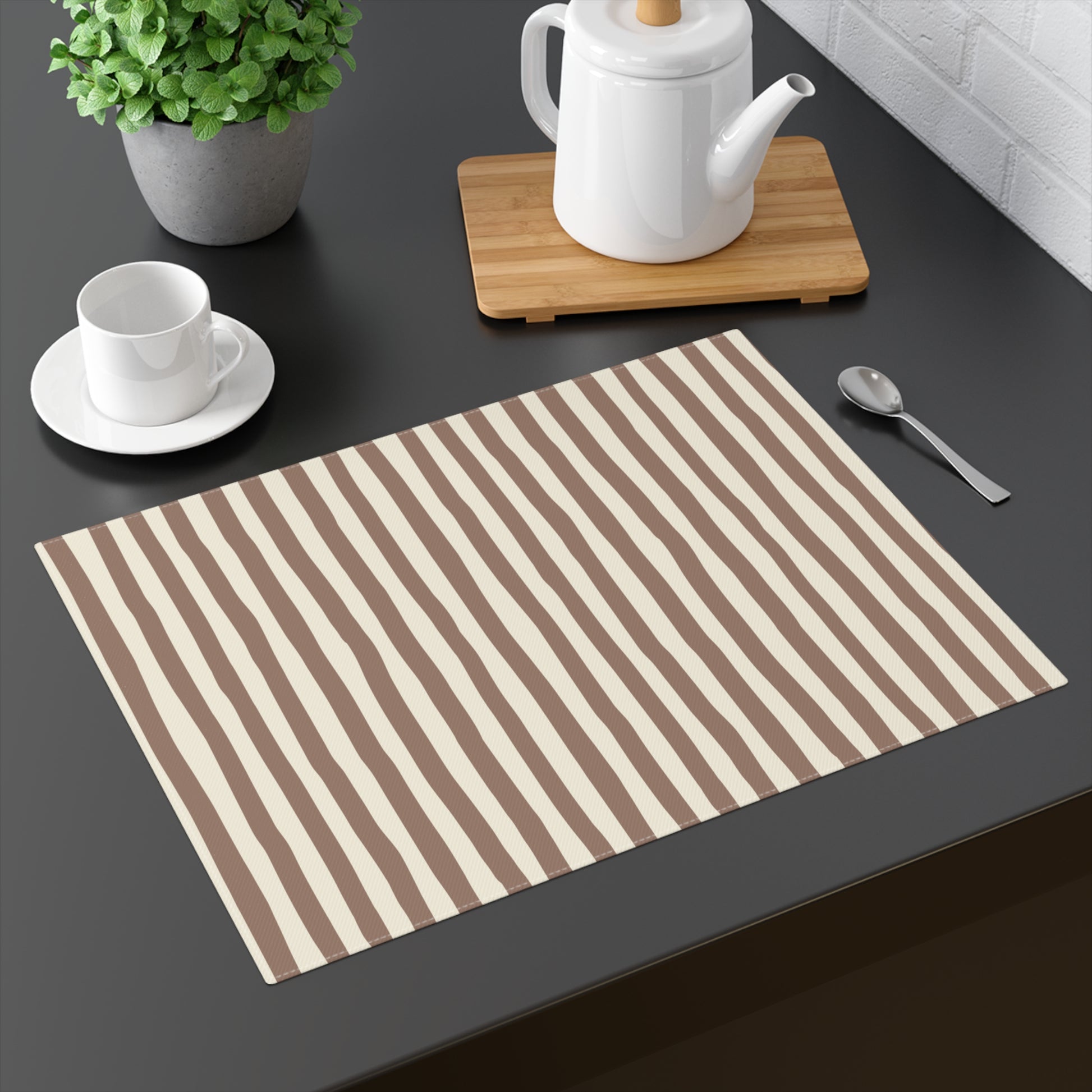 Mocha Striped placemat with brown and beige stripes on a dark surface with a teapot, cup, and spoon.