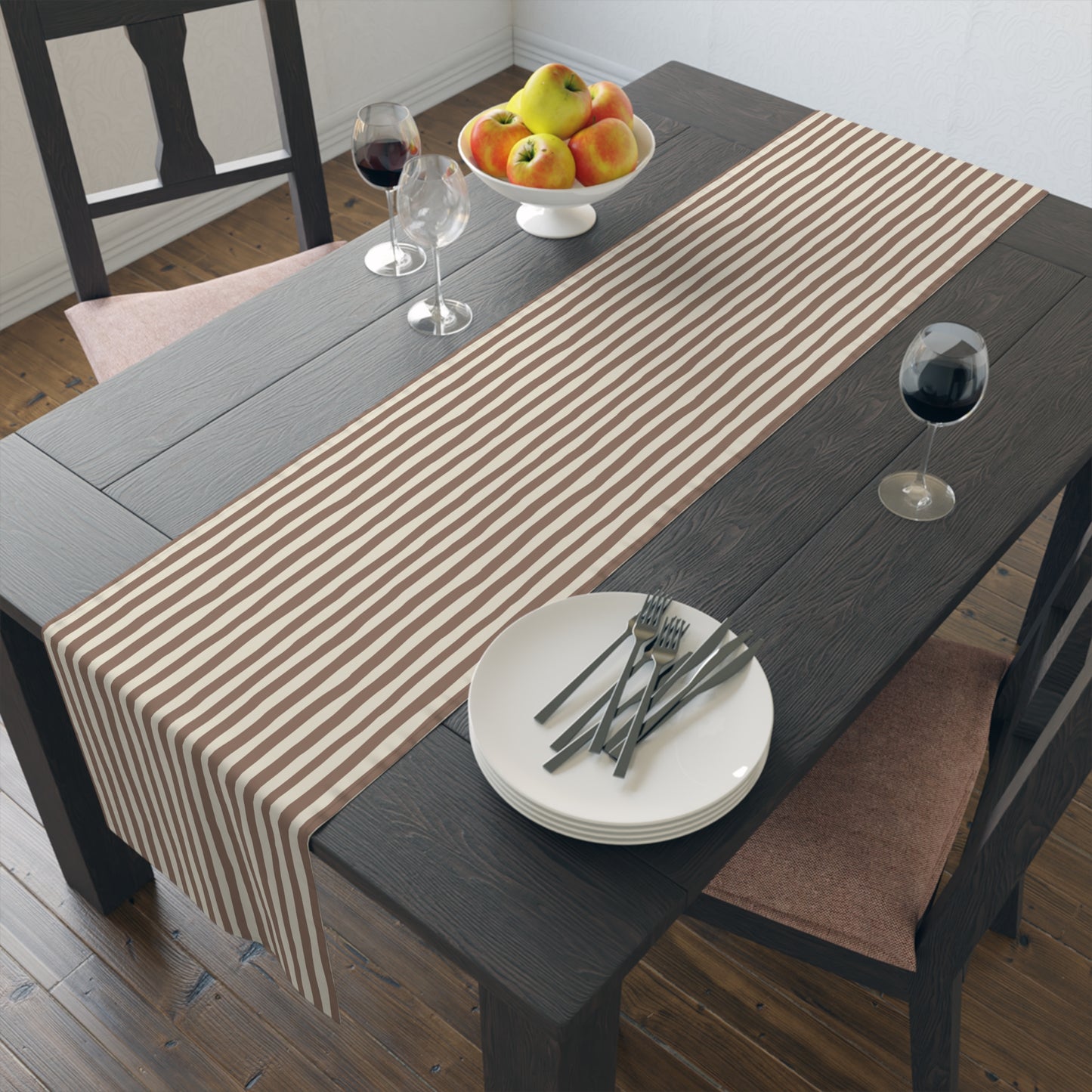 Dining table with a brown and beige striped table runner, plates, and glasses on a wooden floor.