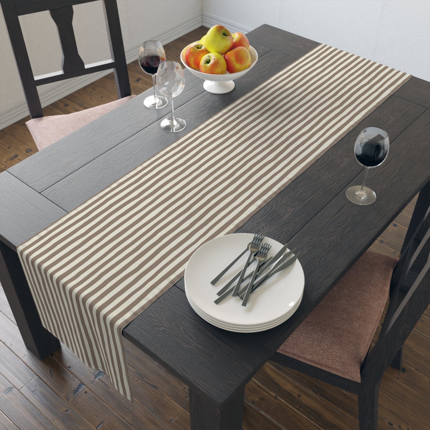 Dining table with a brown and beige striped table runner, plates, and glasses on a wooden floor.