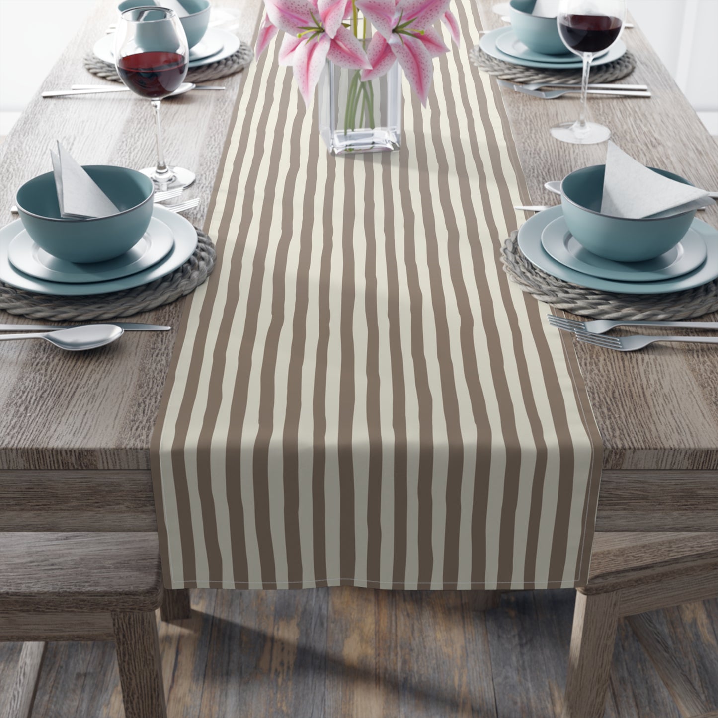 Dining table with a striped brown and beige table runner, plates, bowls, and glasses.