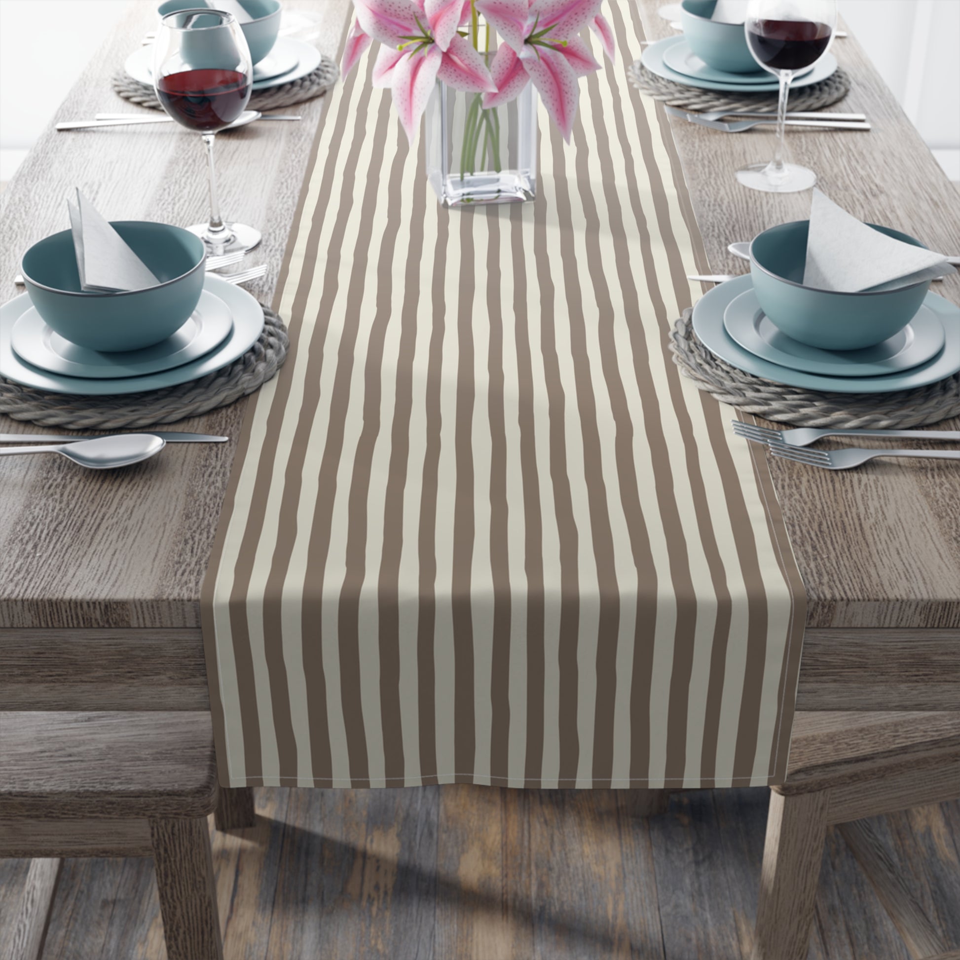 Dining table with a striped brown and beige table runner, plates, bowls, and glasses.
