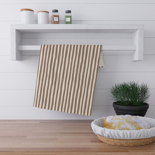 Mocha sriped towel hanging on a rack above a wooden surface with a basket of bread and a plant.