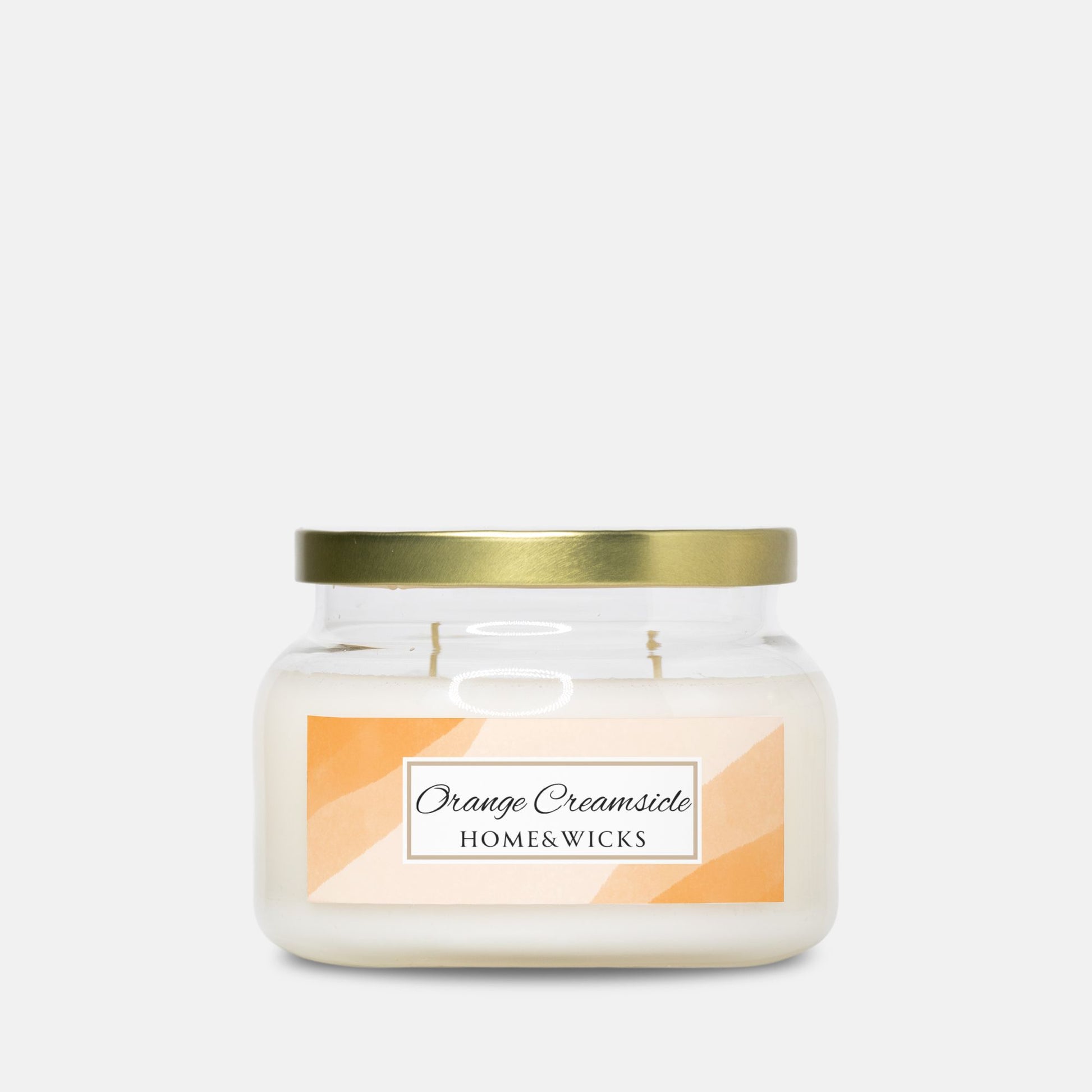 Candle jar with a gold lid and 'Orange Creamsicle' label on a white background