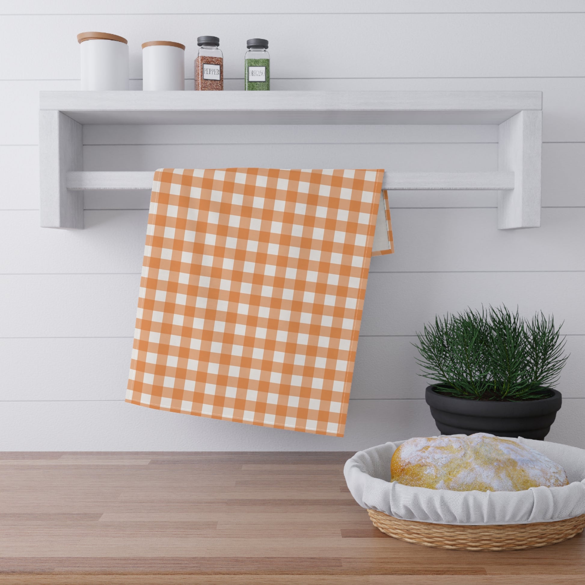 Orange and white gingham checkered towel hanging on a shelf with a plant and basket below.