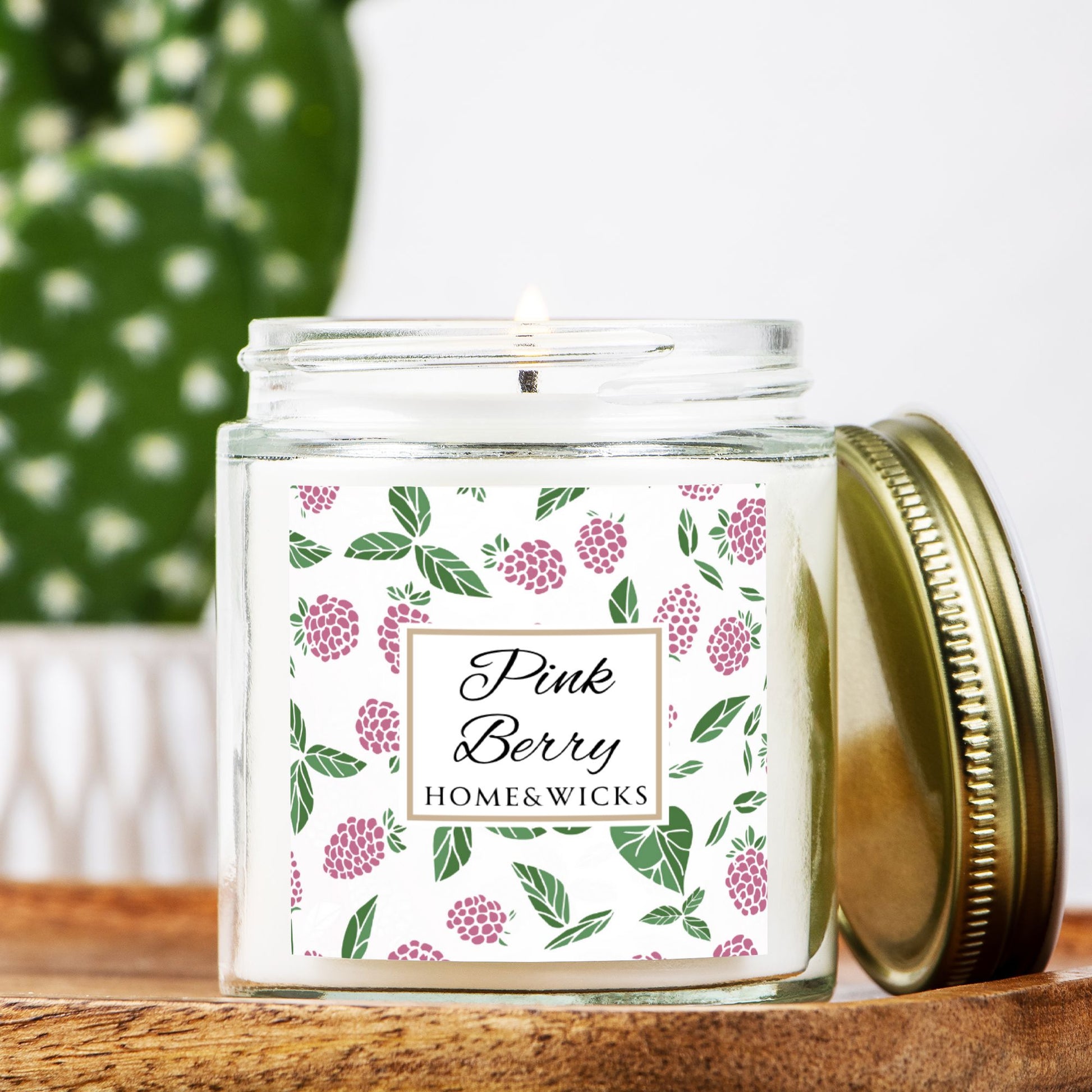 Homes & Wicks Pink Berry candle in a clear jar with gold lid  with pink berry label graphics on a white background on a wooden surface