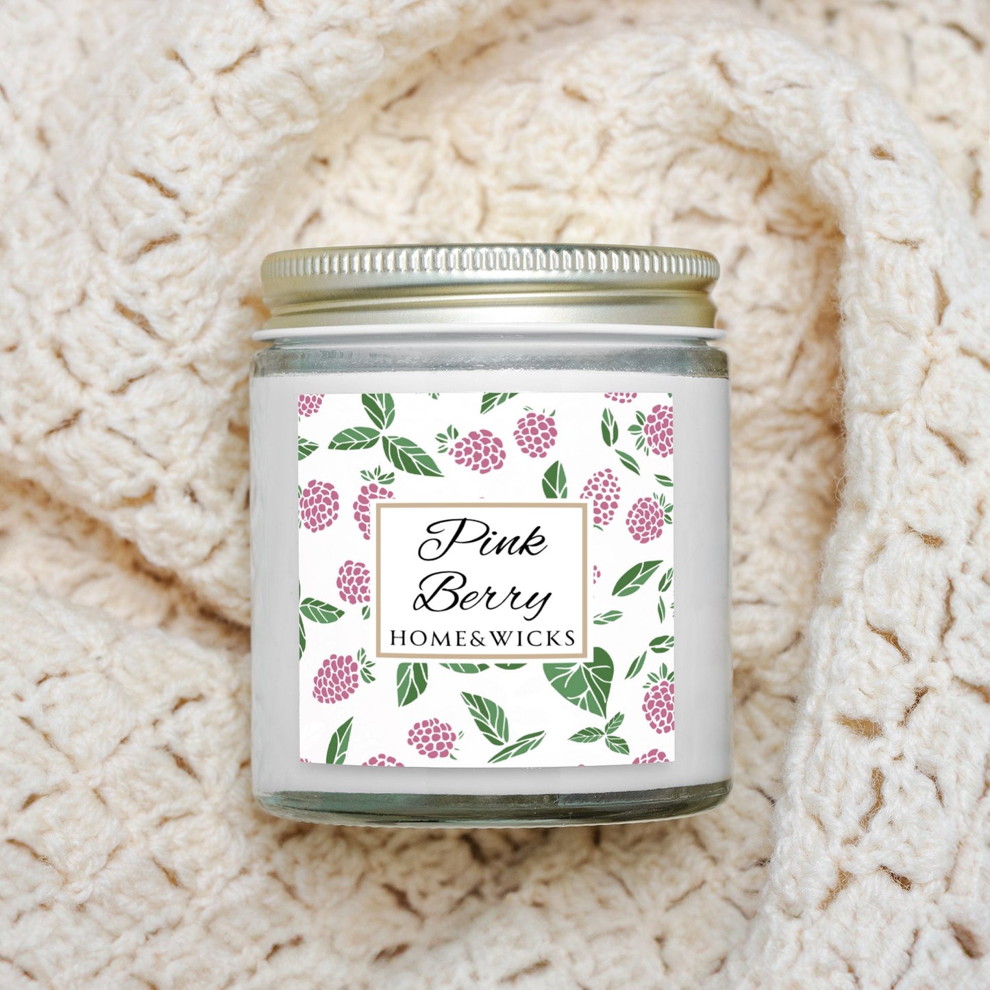 Homes & Wicks Pink Berry candle in a clear jar with gold lid  with pink berry label graphics on a white background on a textured beige blanket background