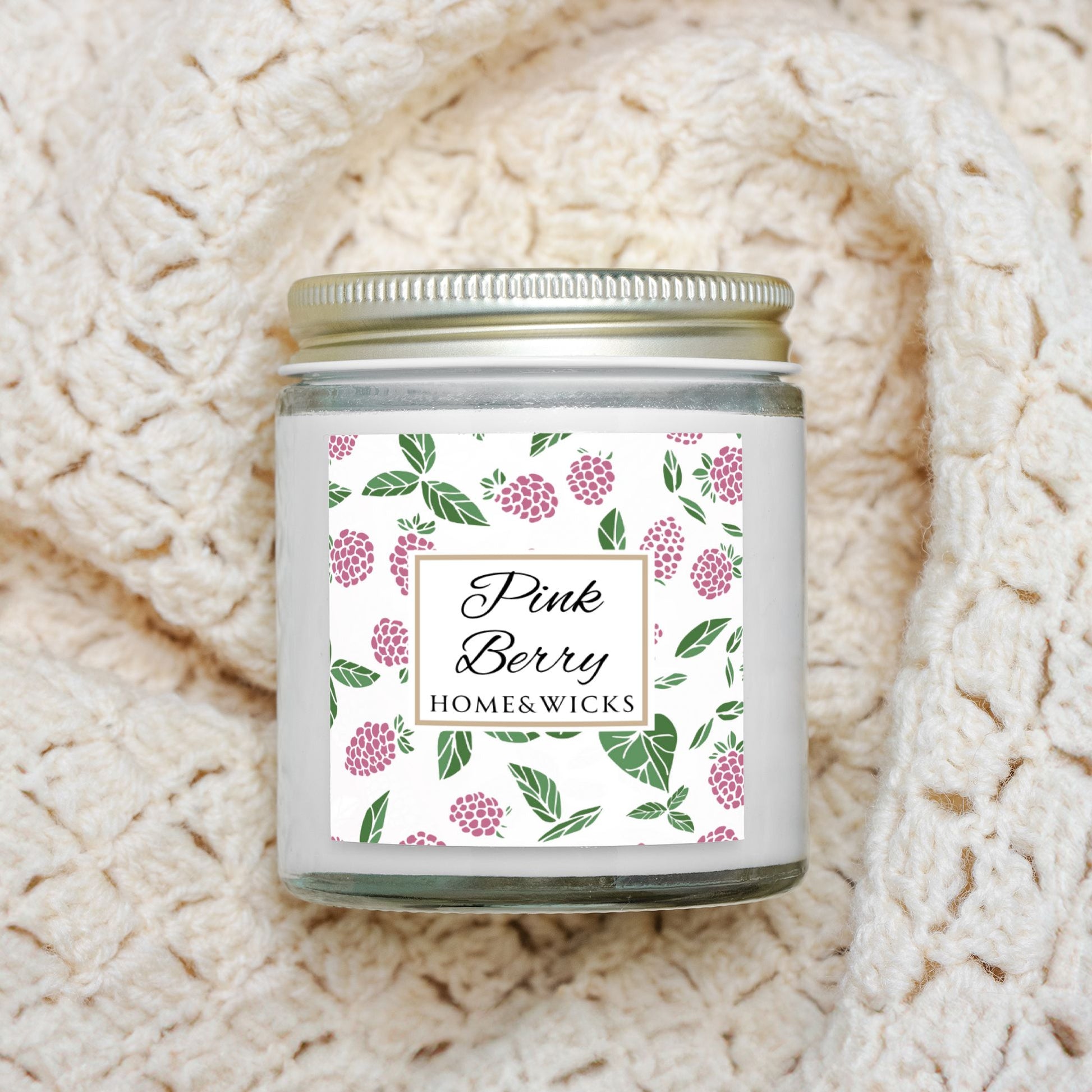 Homes & Wicks Pink Berry candle in a clear jar with gold lid  with pink berry label graphics on a white background on a textured beige blanket background