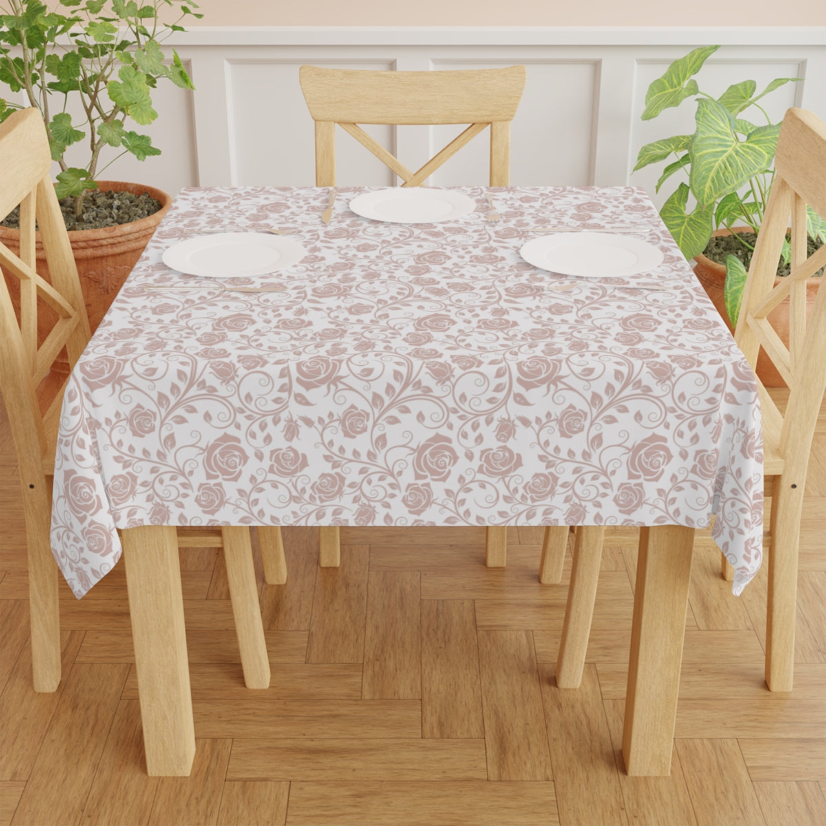 Dining table with a pink & white floral patterned tablecloth, surrounded by wooden chairs, on a wooden floor.