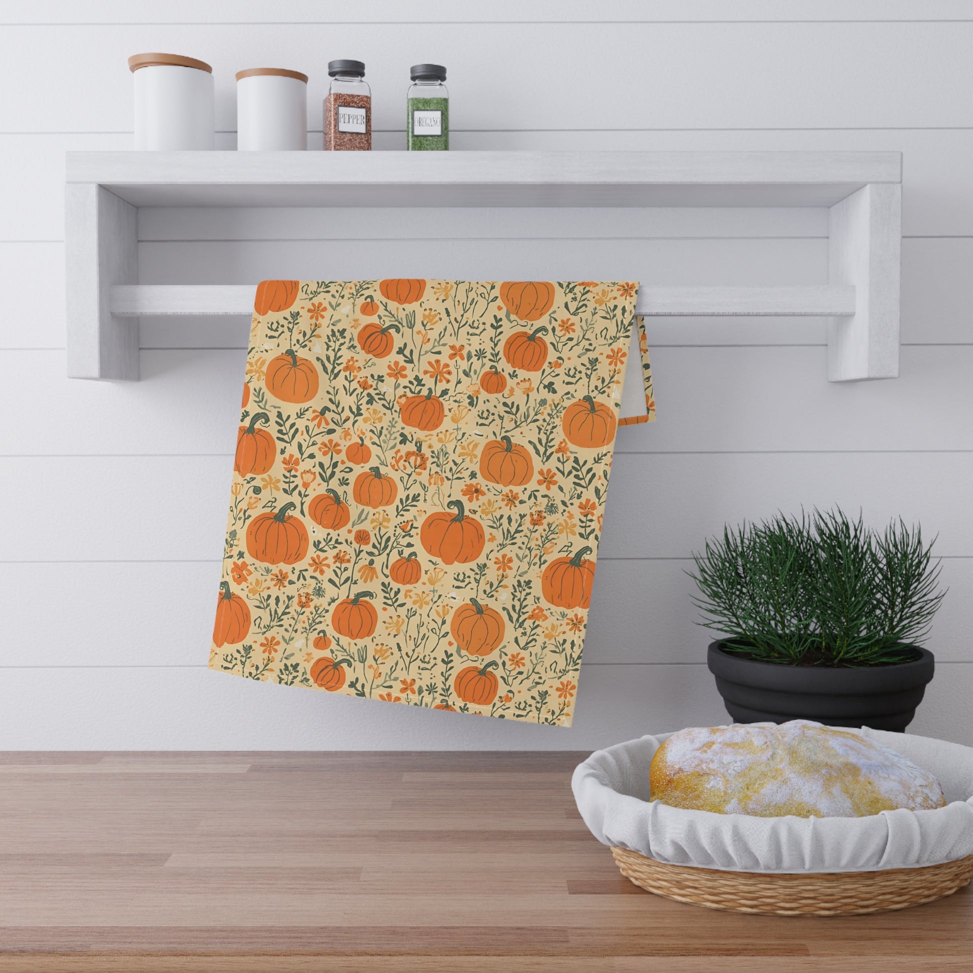 Decorative kitchen tea towel with pumpkin pattern hanging on a wall in a kitchen setting.