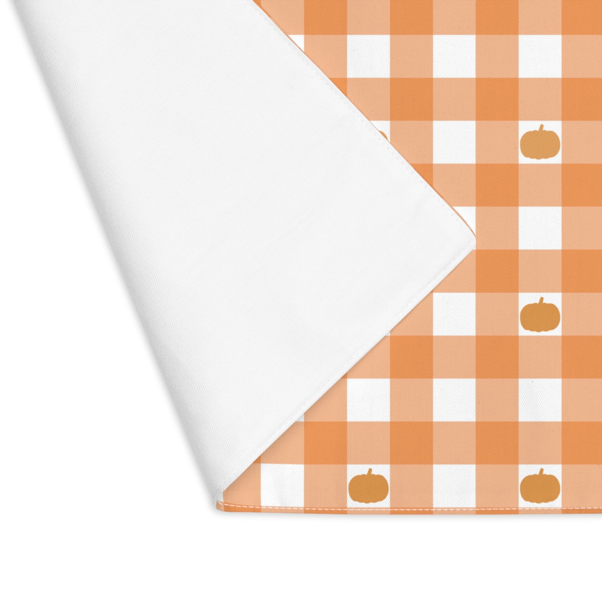 Our Pumpkin Gingham placemat is folded over at the corner to reveal the white back of this orange and white checkered patterned placemat with small pumpkins on the cotton twill placemat fabric on a white background