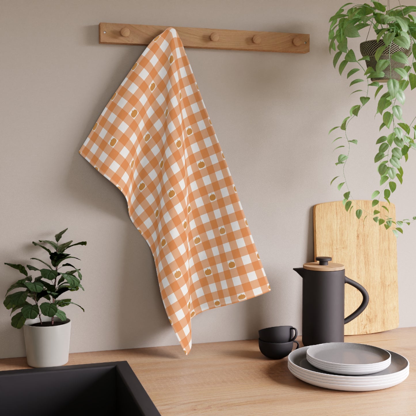 Kitchen scene with an orange and white  checkered gingham pumpkins kitchen tea towel, plants, and kitchenware on a wooden surface.