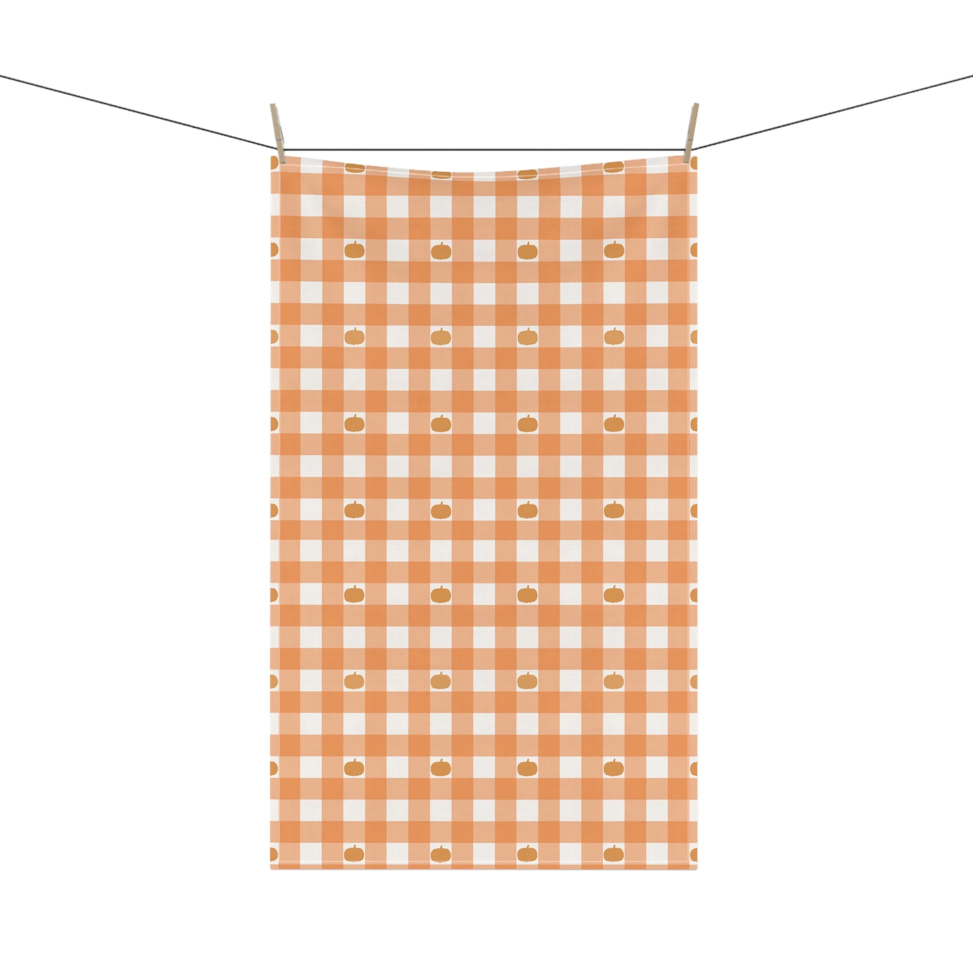 Orange and white checkered kitchen tea towel with pumpkins hanging on a line against a white background