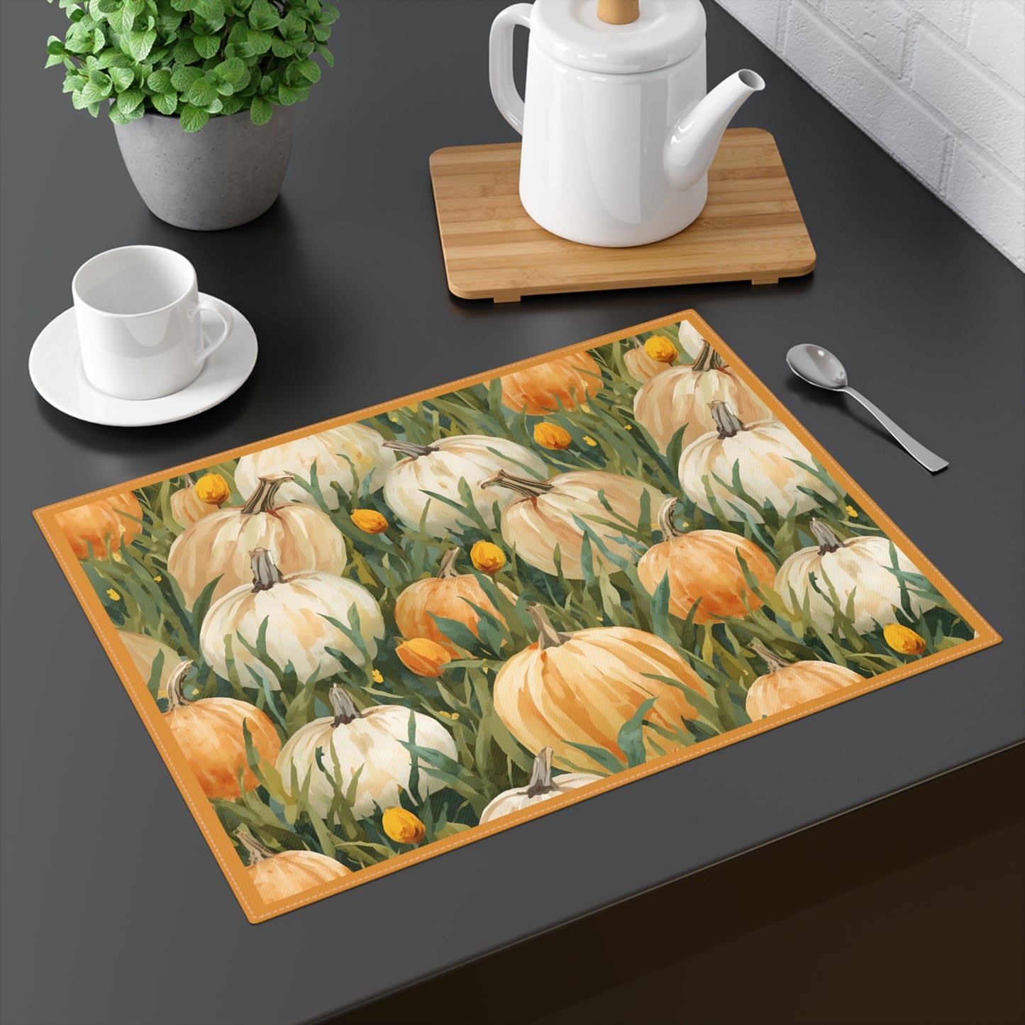 Pumpkin Patch placemat has white and orange pumpkins in grass with orange tulips printed on front of the placemat cotton twill fabric on a dark table with tea pot and tea cup.
