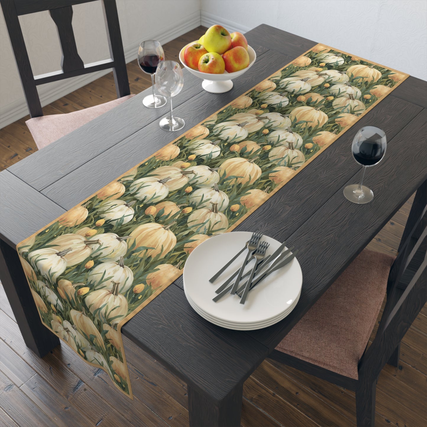 Pumpkin Patch table runner has white and orange pumpkins in grass with orange tulips printed on front of table runner cotton twill fabric and sits on a dining table with plates, cutlery, and fruit on a wooden floor.
