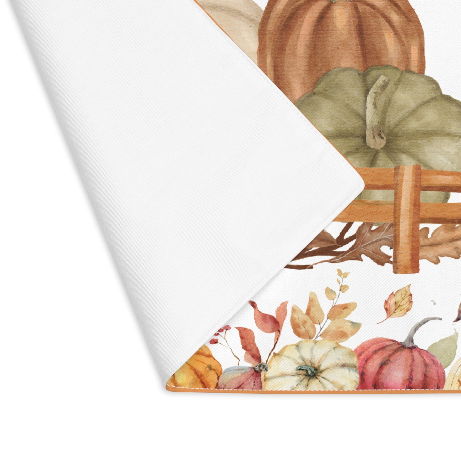 Pumpkins placemat with pumpkins and autumn leaves on the placemat's cotton twill fabric, with one corner folded over to reveal white backside, on a white background