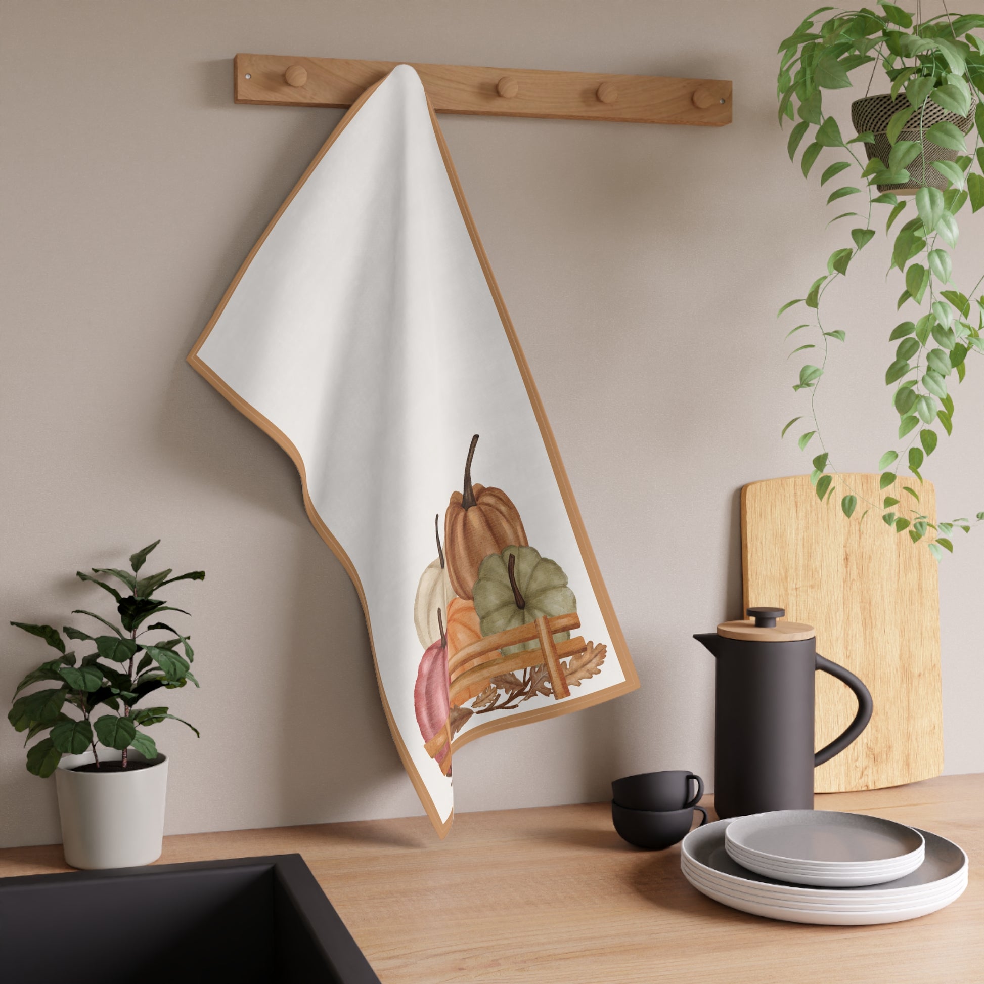 Decorative towel with pumpkin design hanging on a wooden rack in a kitchen setting.