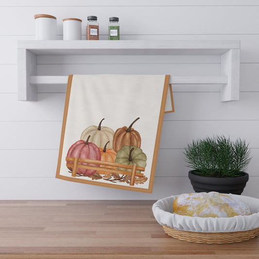 Kitchen towel with pumpkin design hanging on a wall above a wooden shelf.