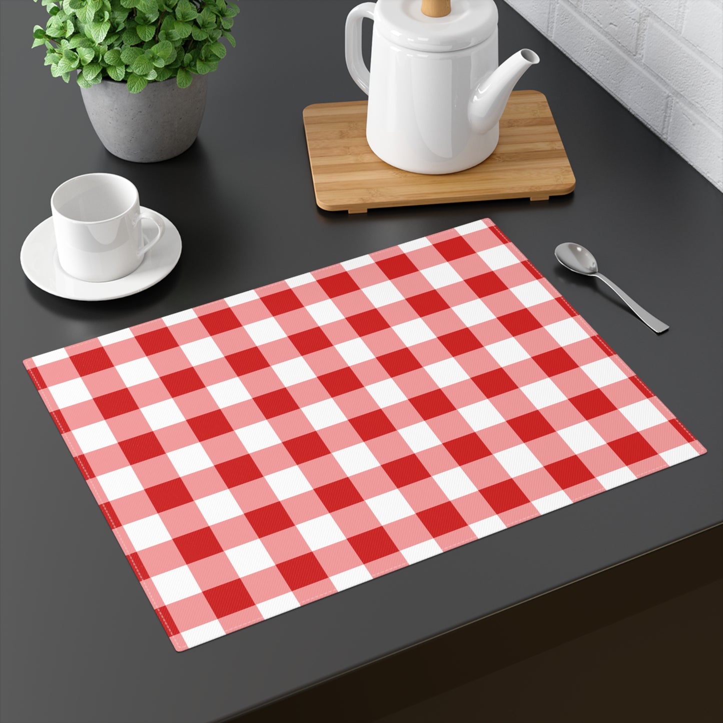 Red gingham placemat with red and white checkered pattern on a dark table with teapot and tea cup.