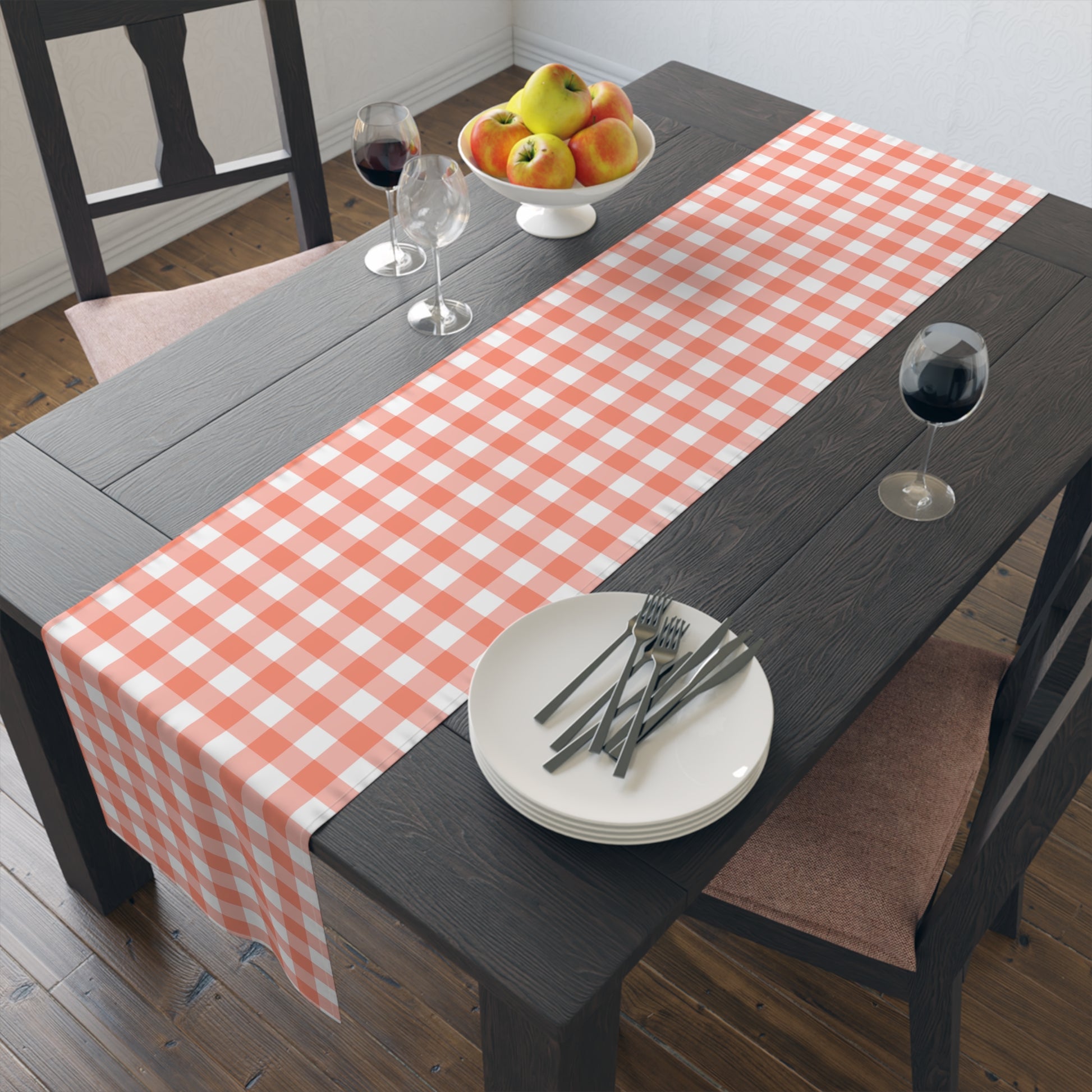 Dining table with a gingham checkered table runner, plates, forks, and a fruit bowl.