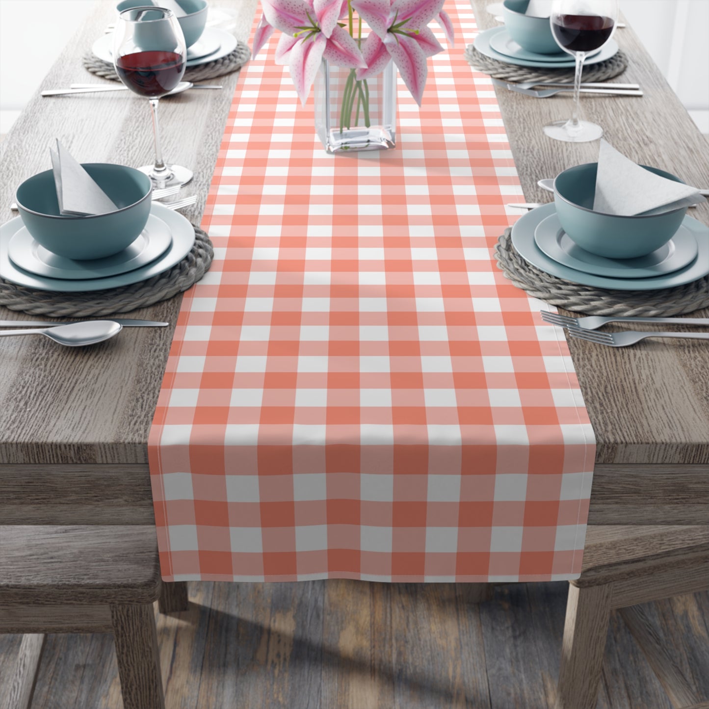 Dining table set with a gingham checkered table runner, blue bowls, and pink flowers.