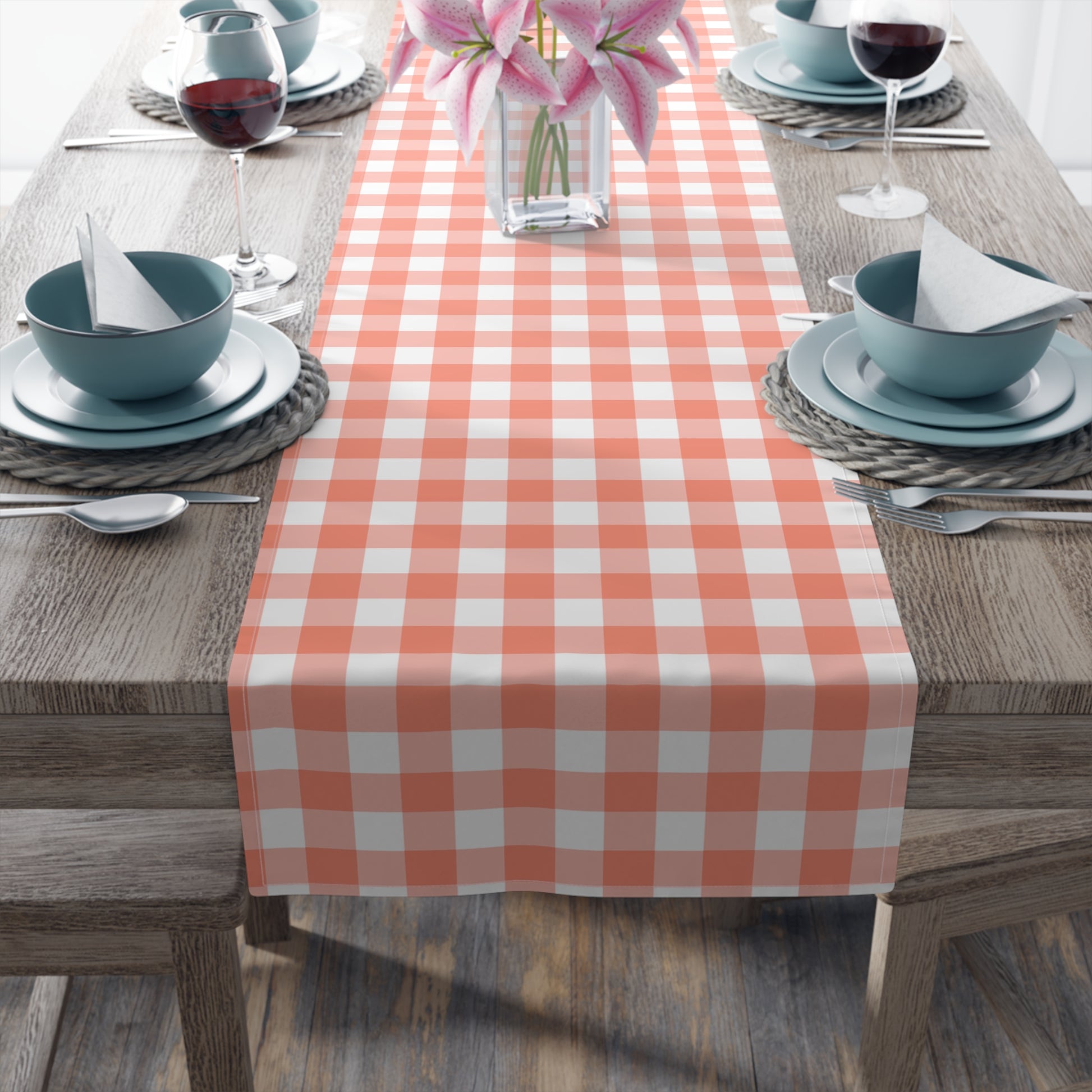 Dining table set with a gingham checkered table runner, blue bowls, and pink flowers.