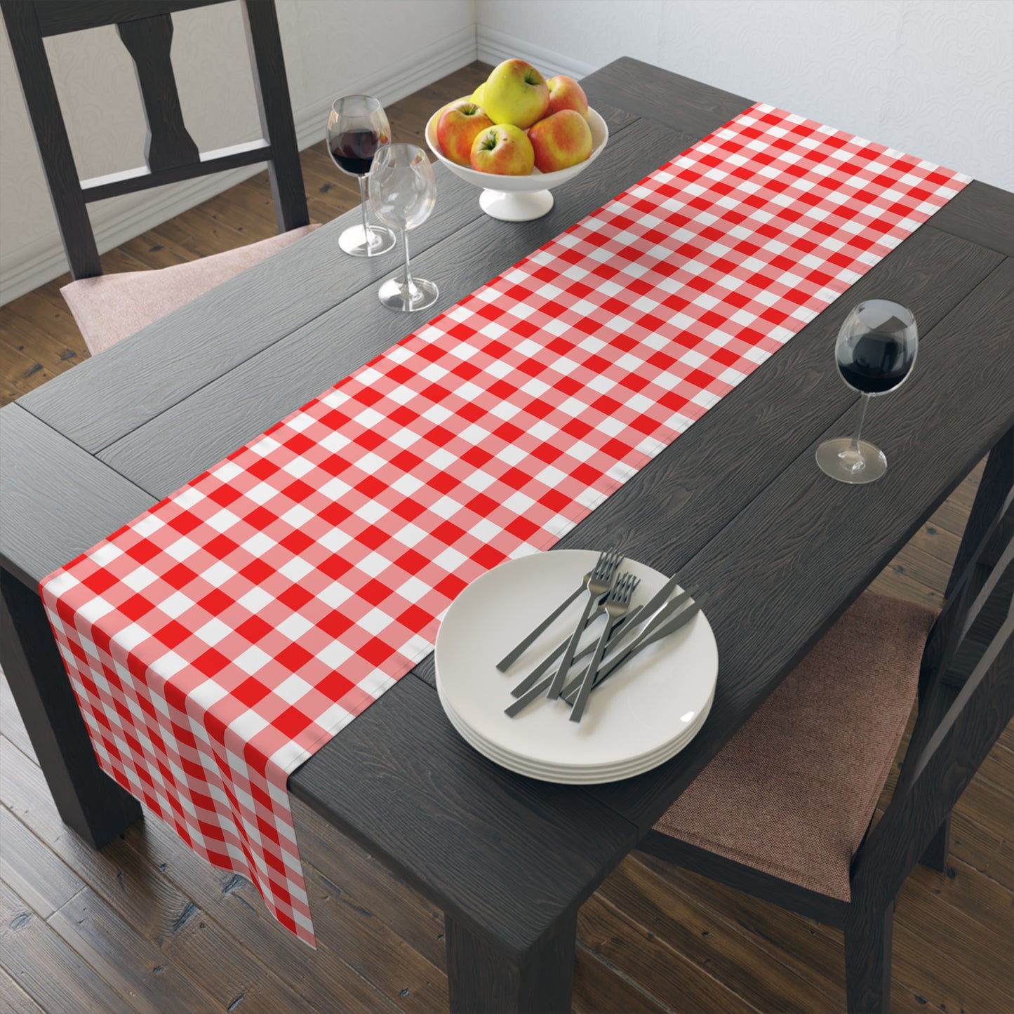 Dining table with a red and white gingham checkered table runner, plates, forks, and glasses.