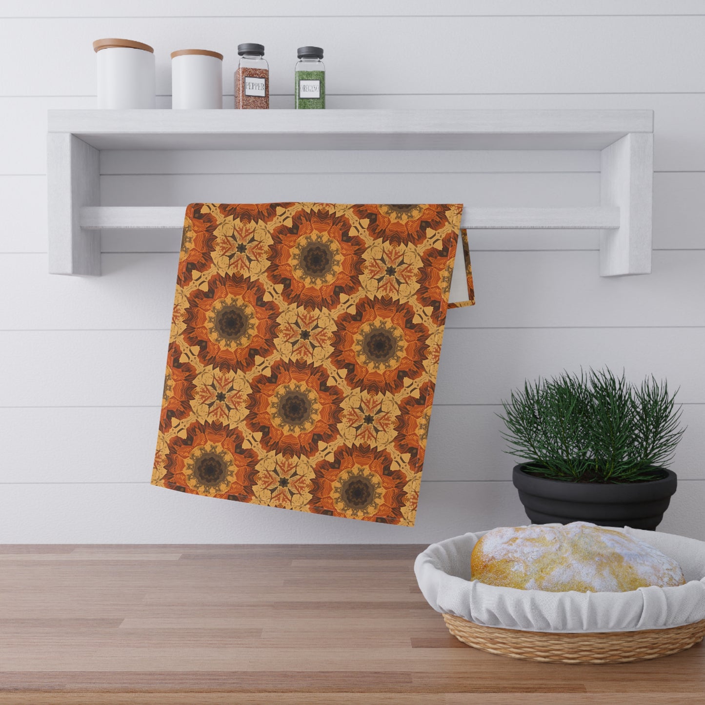 Decorative towel with orange tye-dye floral pattern on a wooden surface with a plant and basket in the background.