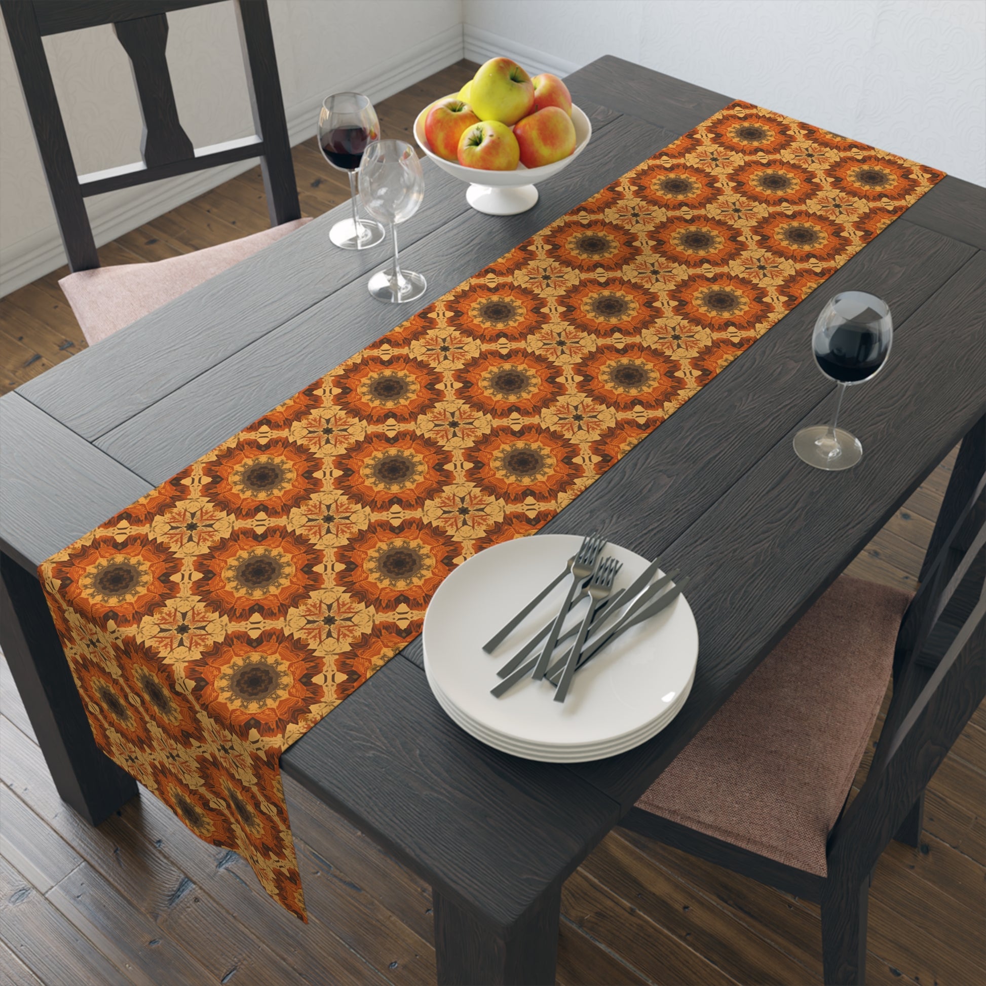 Dining table with a orange, gray and yellow tye-dye patterned table runner, plates, forks, and a fruit bowl.