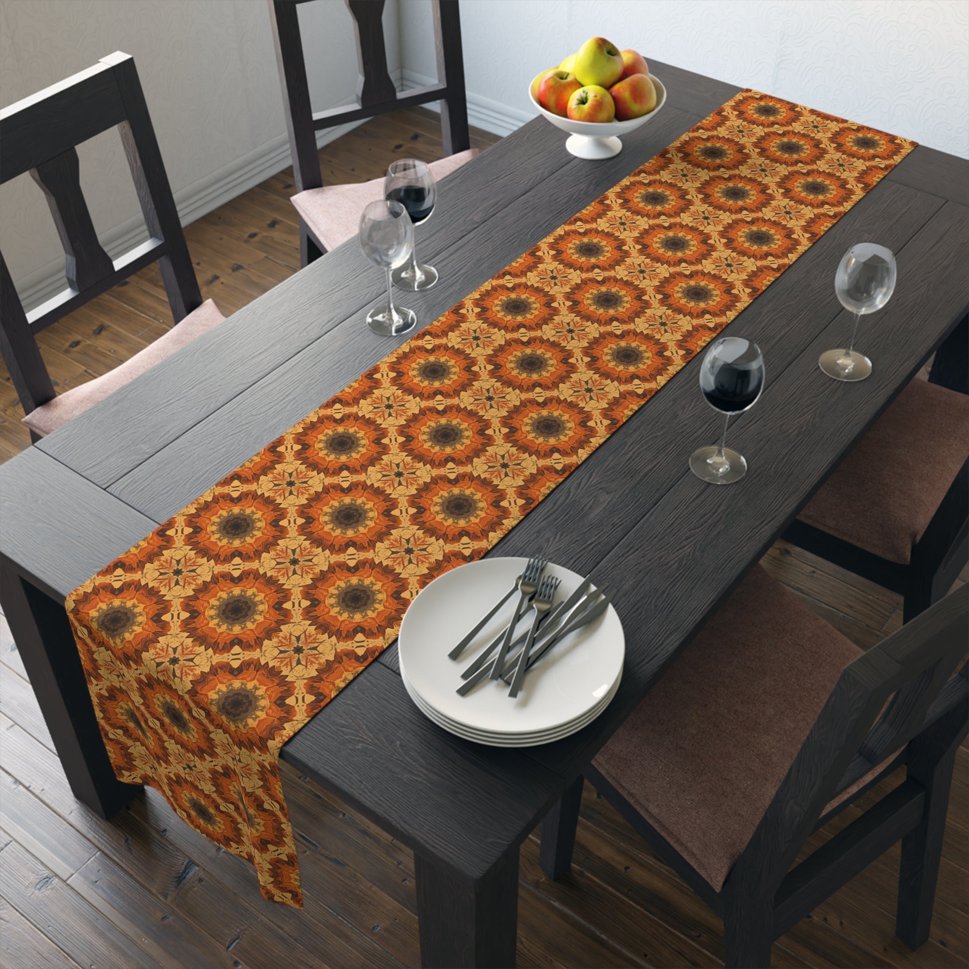 Dining table with a tye-dye orange, yellow and gray patterned table runner, plates, and glasses in a room.