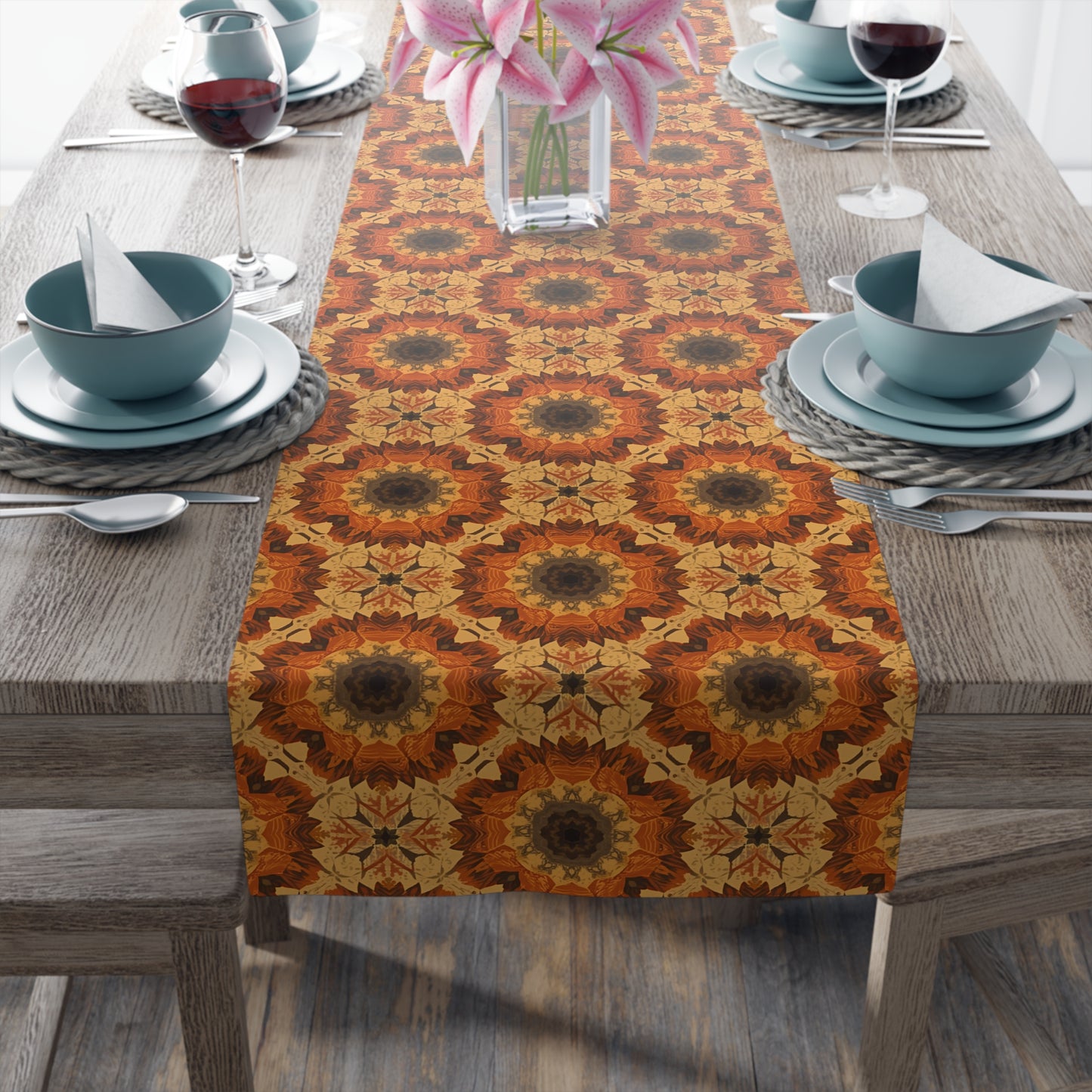 Decorative polyester table runner with orange, gray and yellow geometric tye-dye pattern on a wooden table with place settings.
