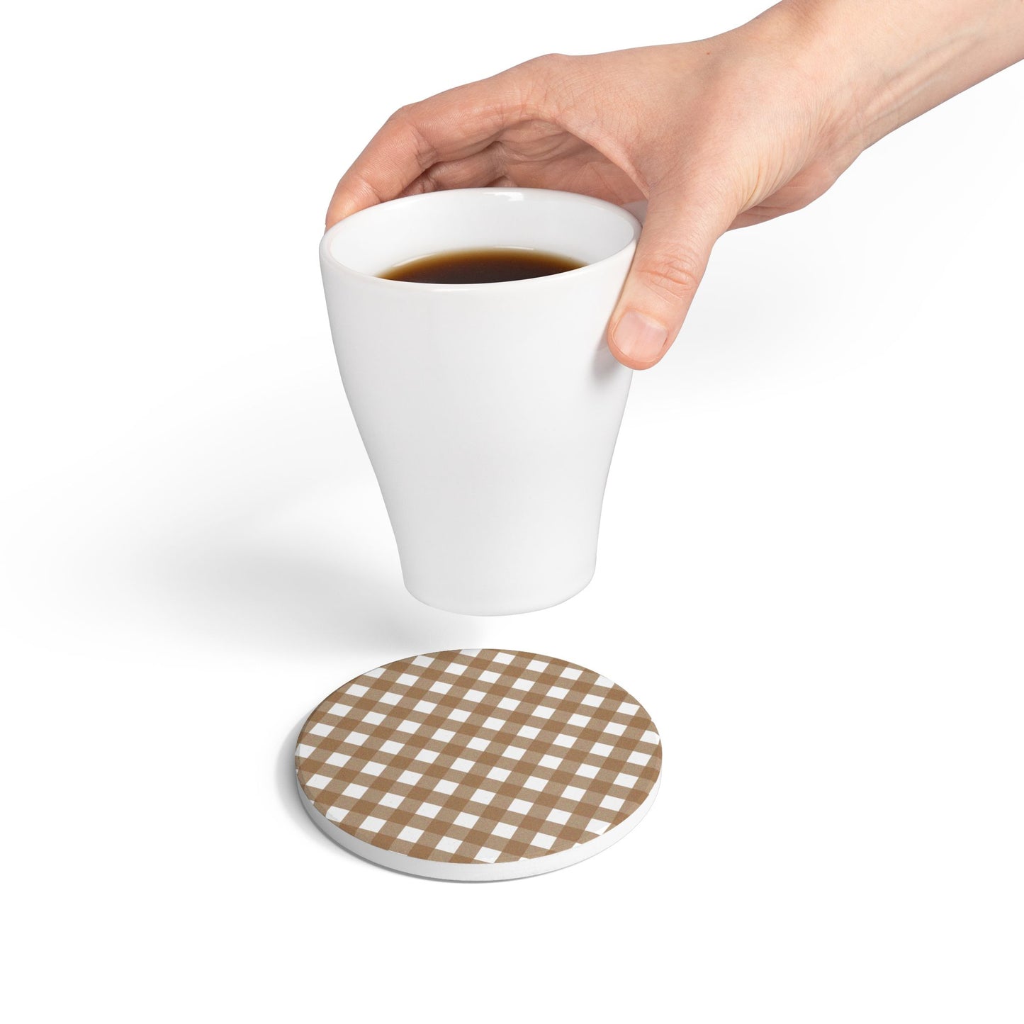 Hand holding a white mug with coffee above a round brown gingham checkered coaster.