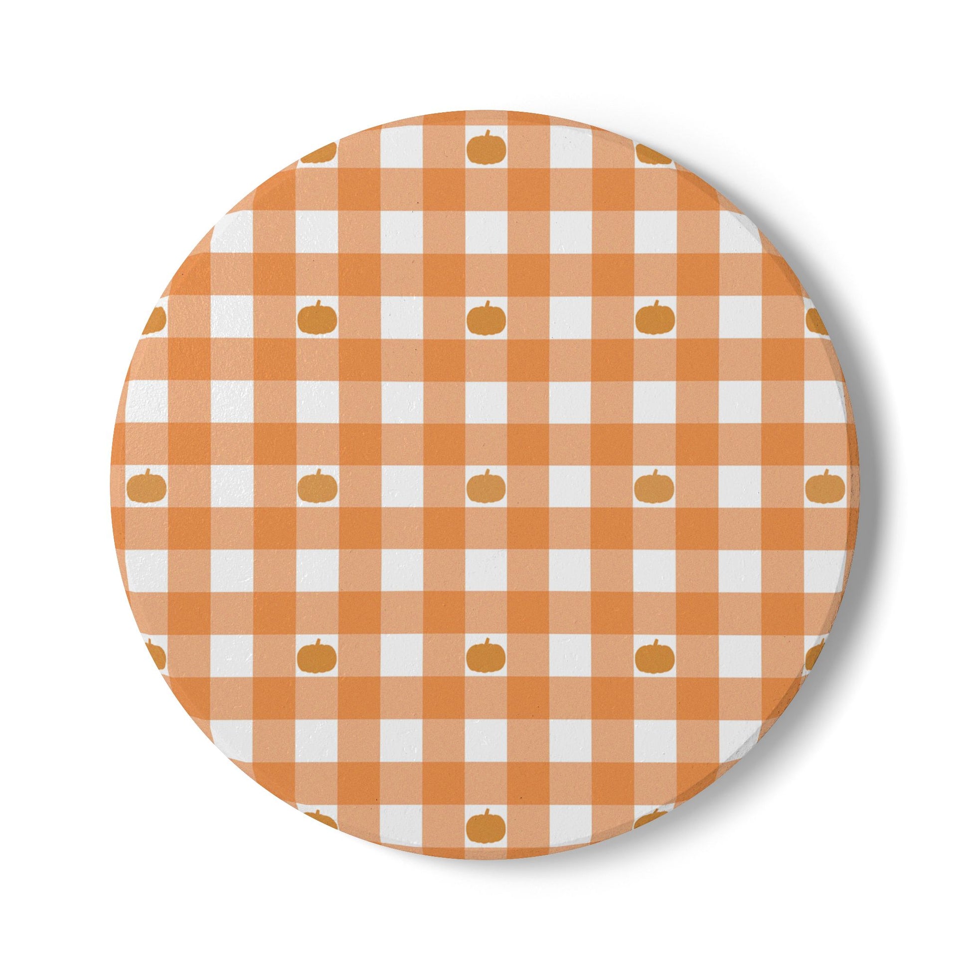 Round ceramic tile coaster with orange and white gingham checkered pattern and small pumpkin icons on a white background