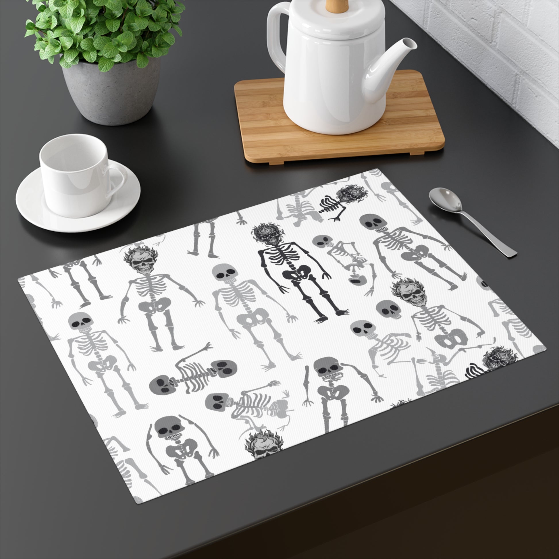 Skeletons placemat with black and white skeleton pattern on front of placemat, on a dark table with a teapot and cup.