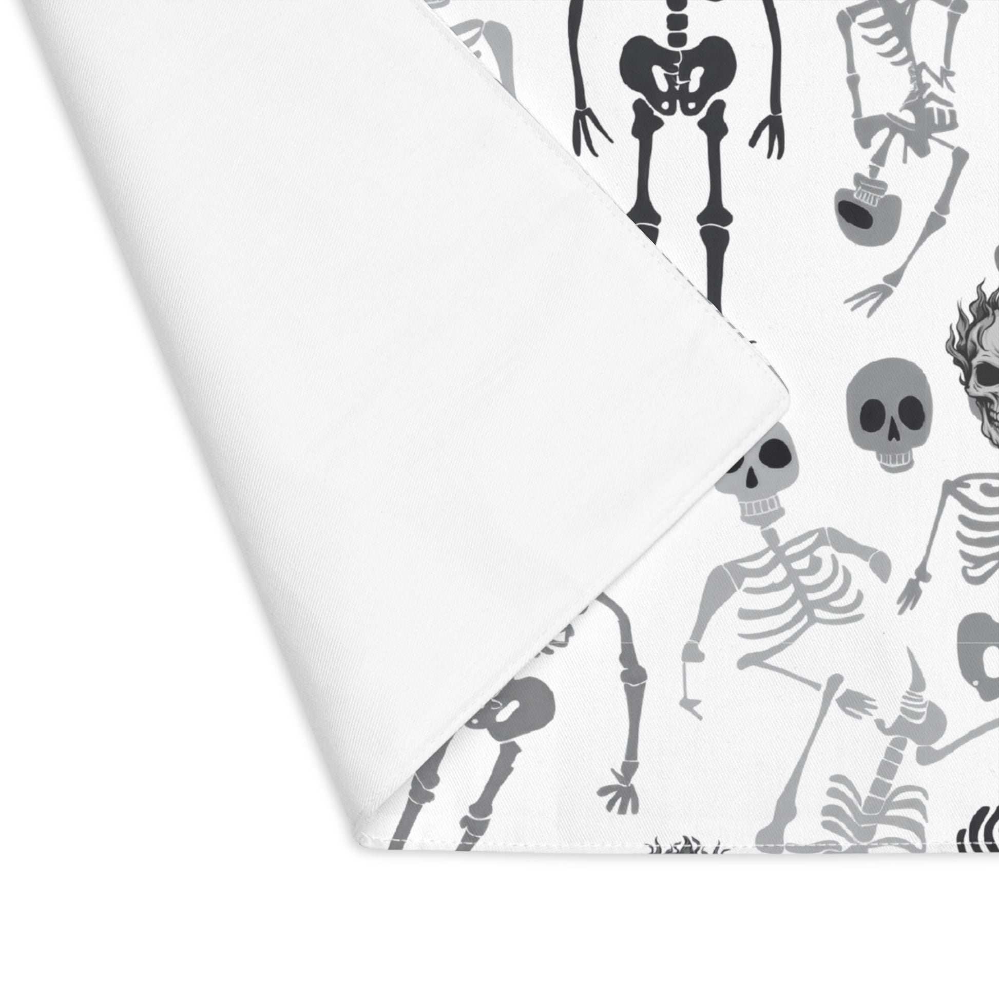 Skeletons placemat with black and white skeleton pattern on front of placemat, with corner folded over to reveal white backside, on a white background.