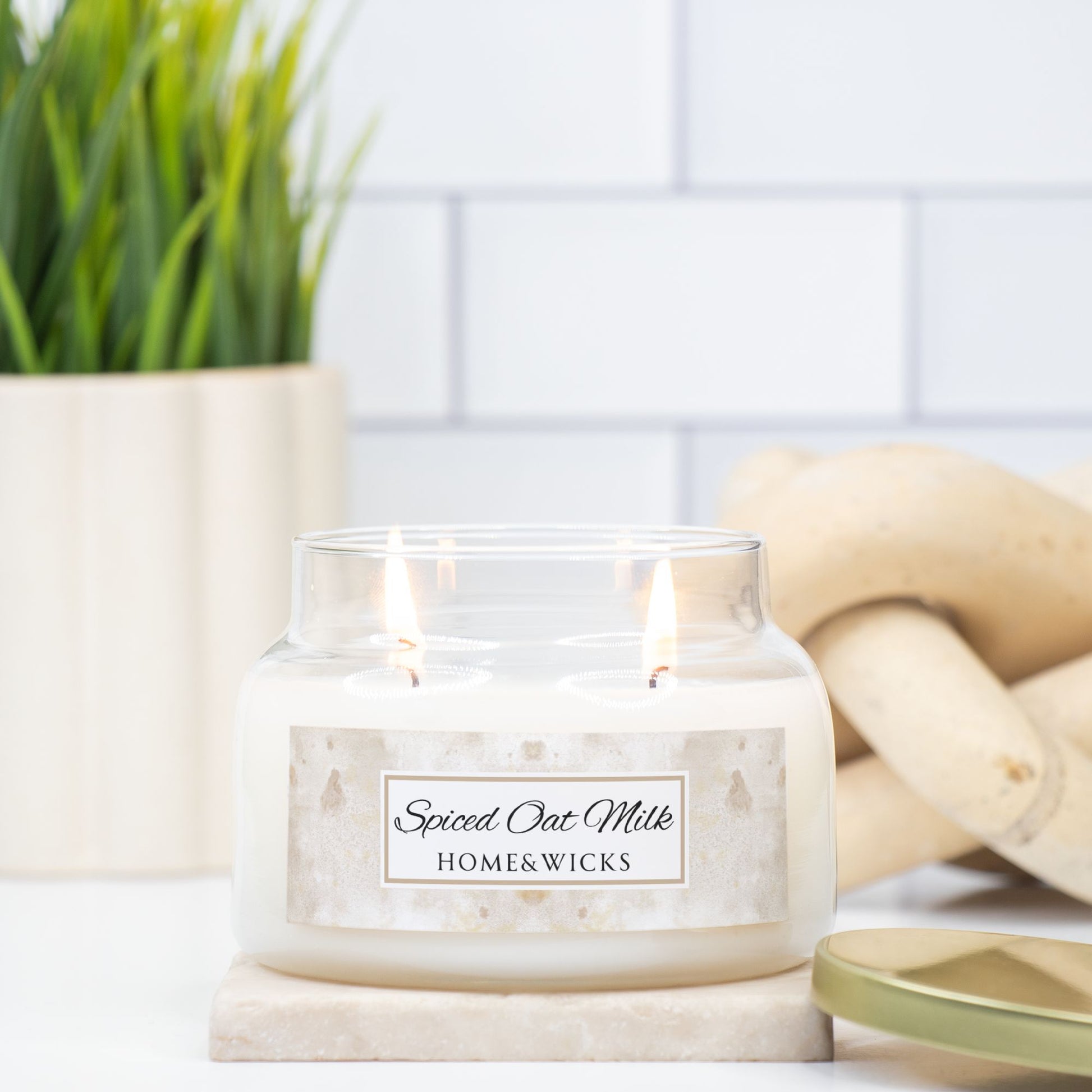 Candle labeled 'Spiced Oat Milk' from HOME & WICKS on a marble surface with a plant and wooden elements in the background.