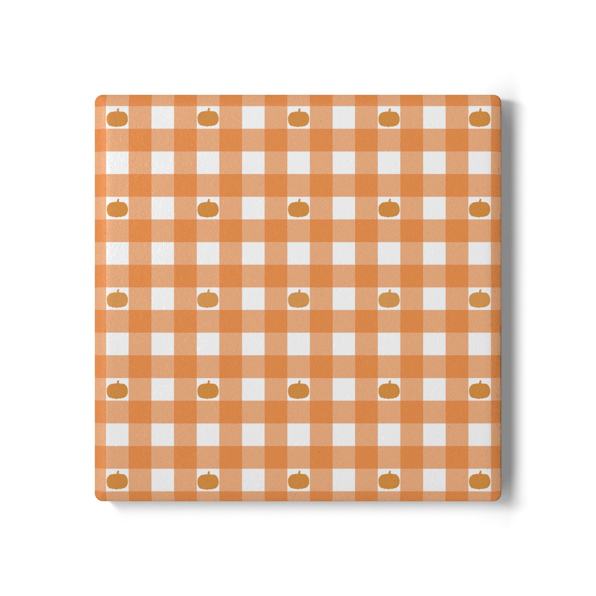 Checkered orange gingham with small pumpkins pattern on a square ceramic tile coaster on a white background.