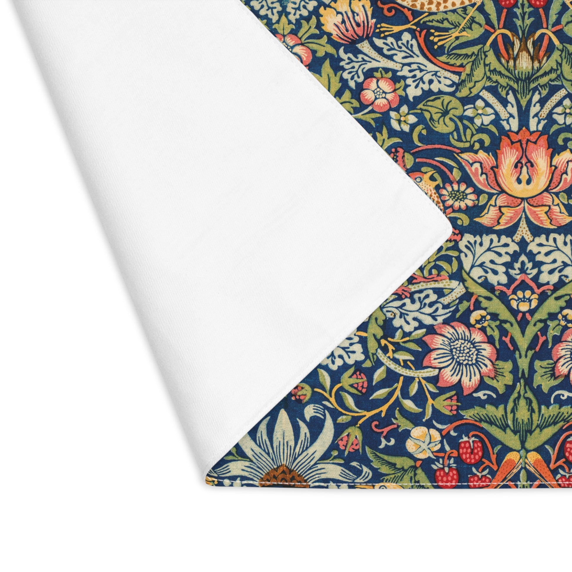 Cotton twill placemat that has the Strawberry Thief illustration by William Morris with a blue background printed on the front of the placemat, on a white background with one corner of the placemat folded over to reveal the white backside
