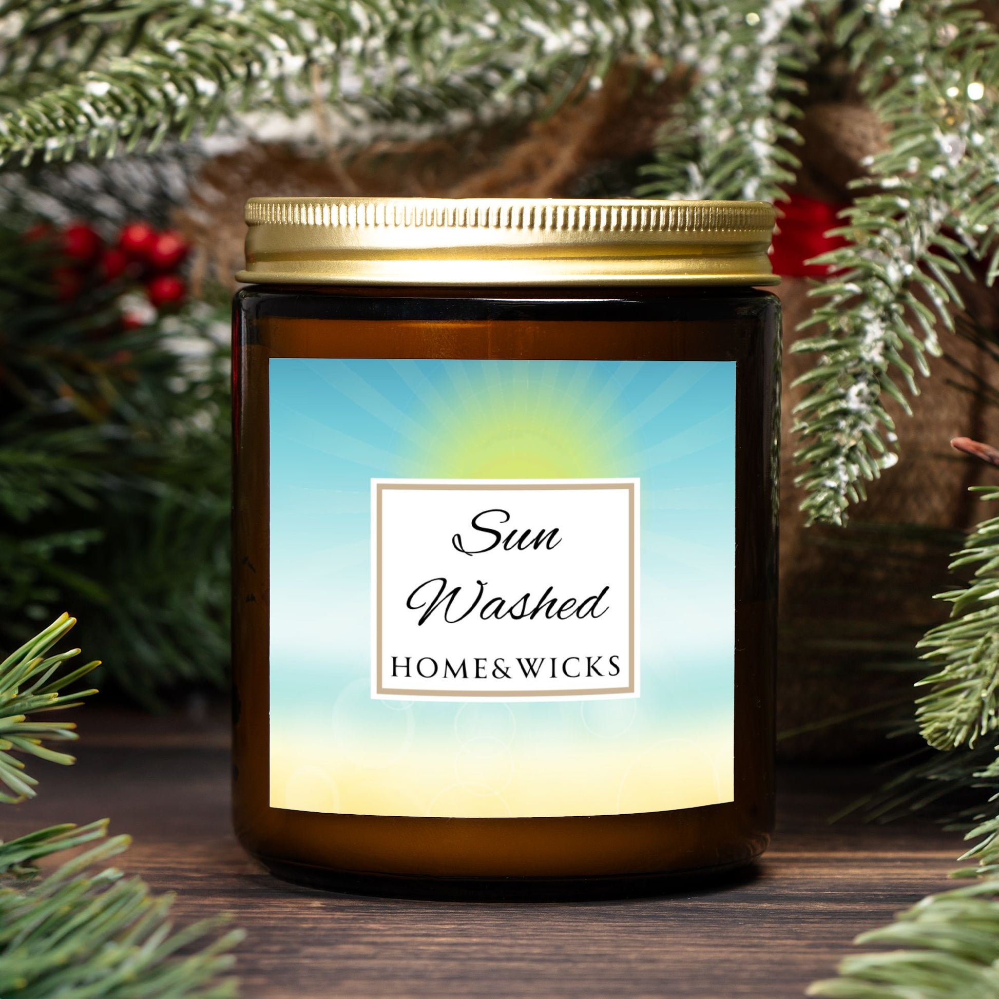 Candle in a 9 oz. amber jar with gold lid with 'Sun Washed' label on with sun graphic gradient background by Home & Wicks, surrounded by greenery
