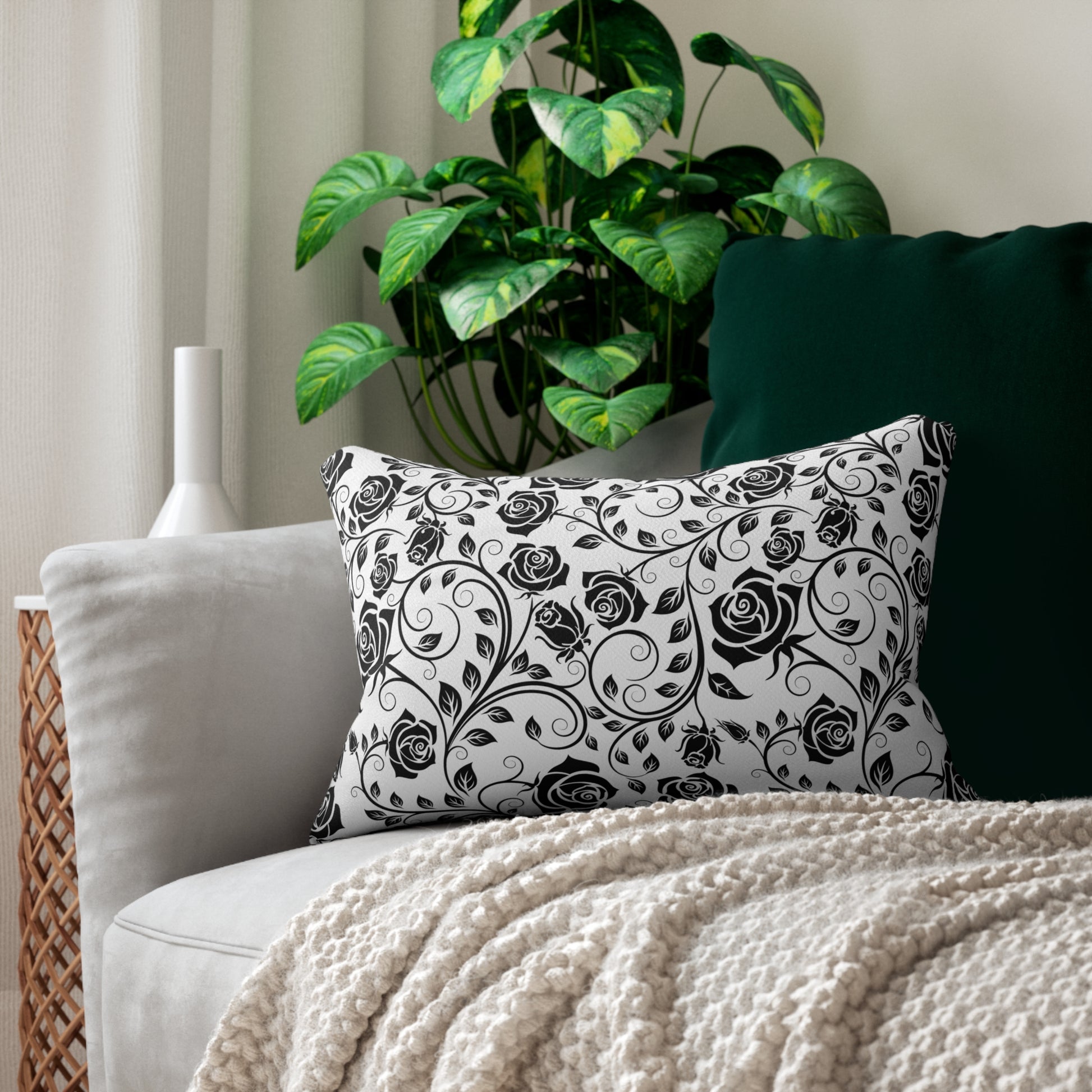 Decorative pillow with black floral pattern on a couch with a plant in the background