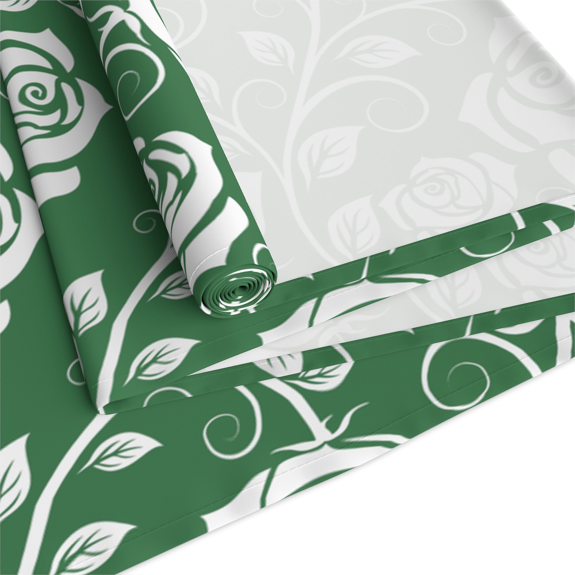 Green and white table runner patterned with floral designs rolled up and folded on a white background