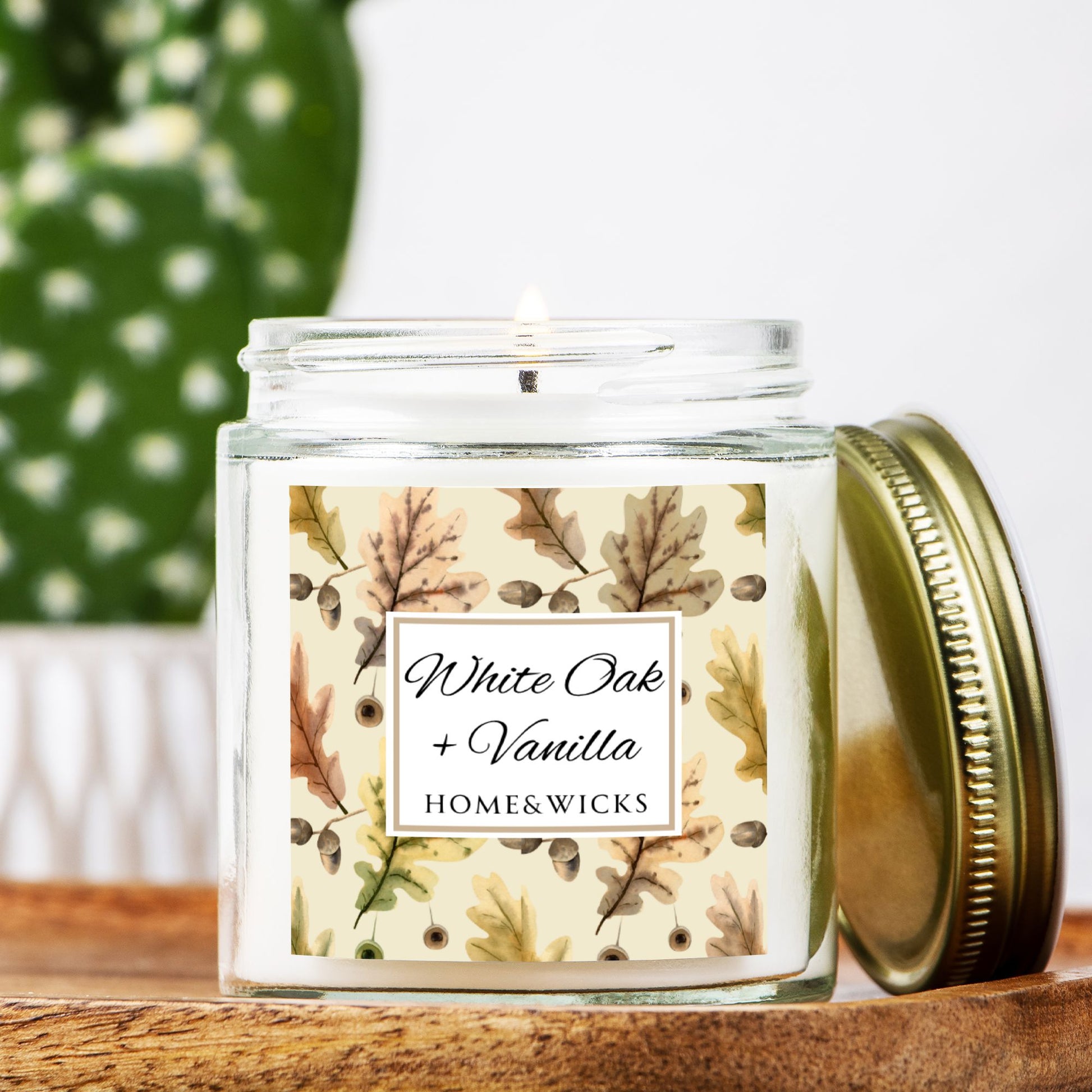 White Oak & Vanilla candle in a 4 oz. clear jar and gold lid with a decorative oak leaf design label featuring leaves and the brand 'Home & Wicks' on a wooden surface