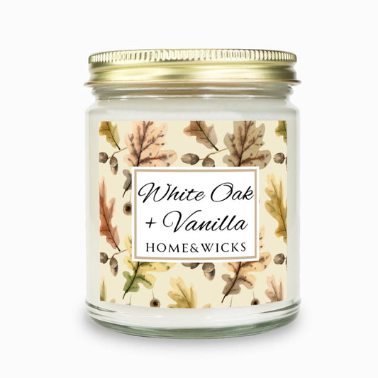 Fall or Thanksgiving candle, "White Oak Vanilla" candle in a clear jar with a gold lid labeled 'White Oak + Vanilla' with oak leaves by Home & Wicks on a white background