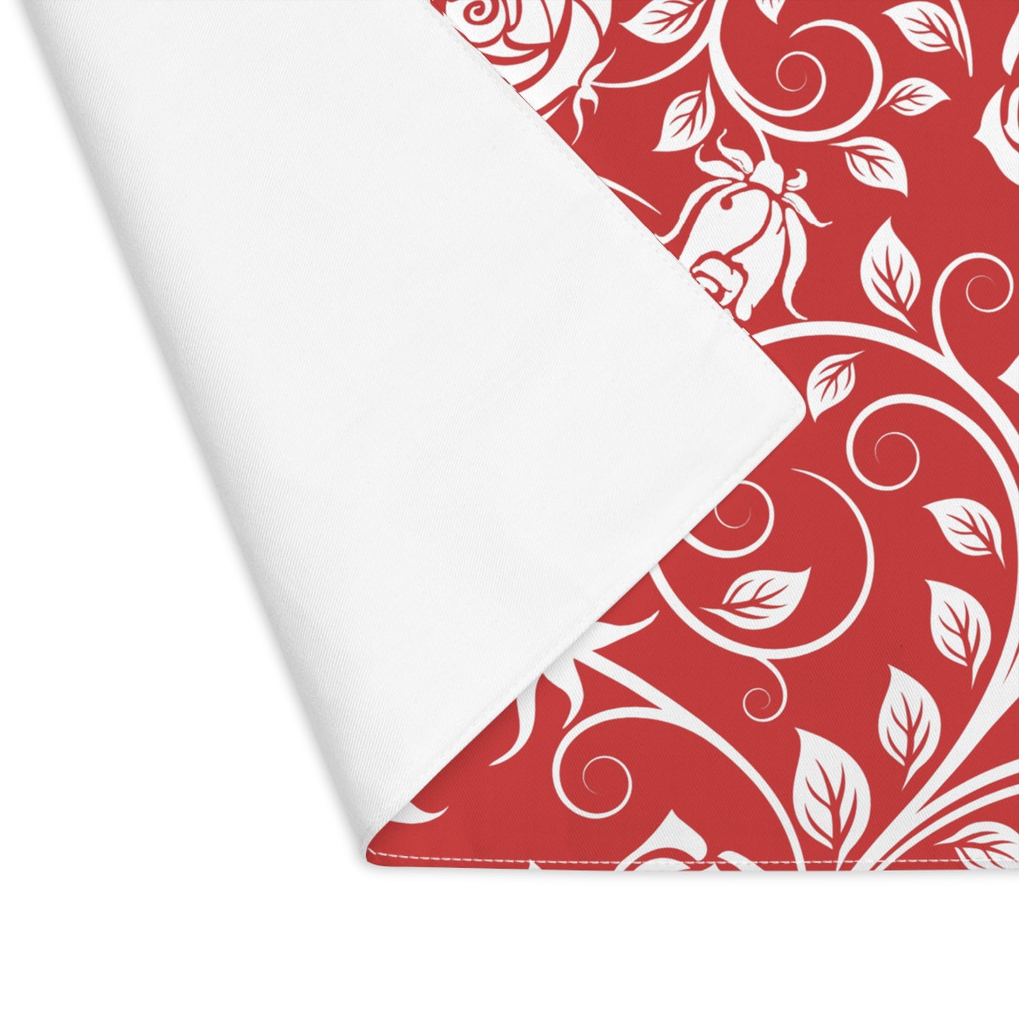 Red and white floral patterned placemat with a corner folded over on one corner to reveal white backside with a white background