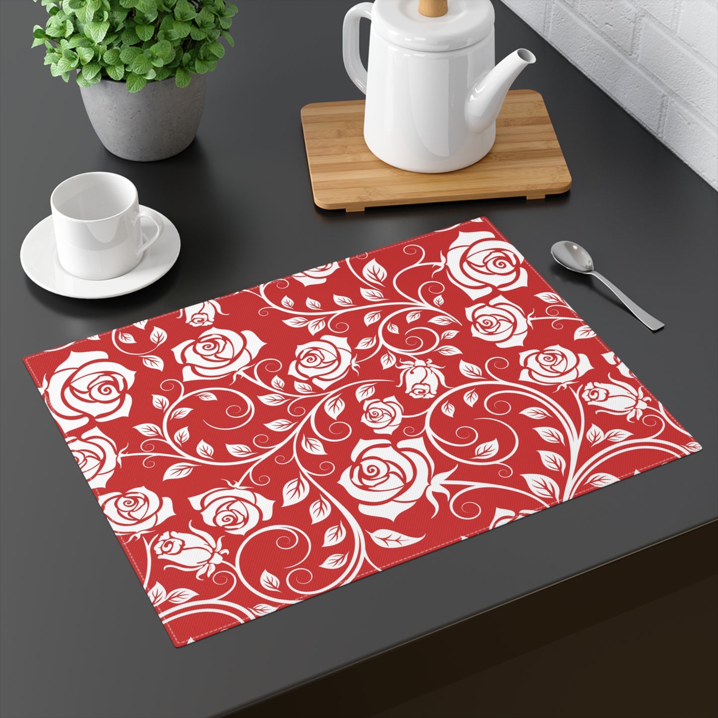 Red placemat with white rose pattern on a dark surface with tea set.