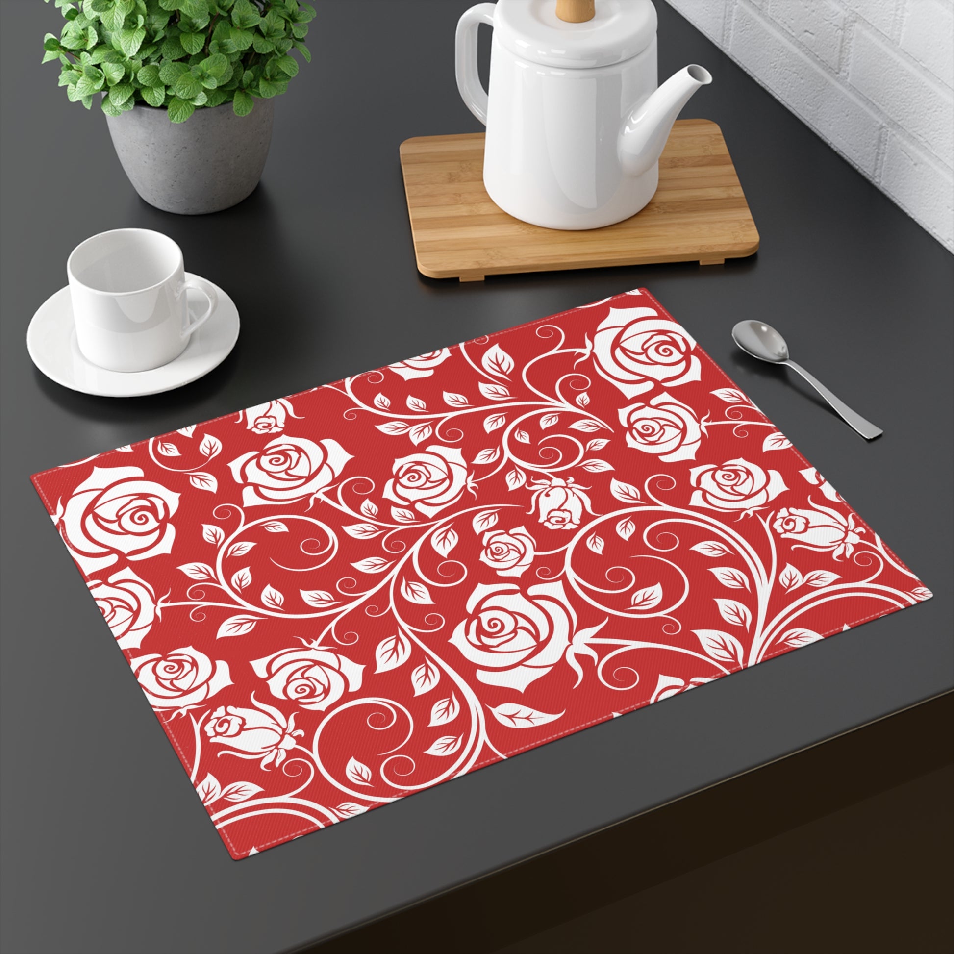Red placemat with white rose pattern on a dark surface with tea set.
