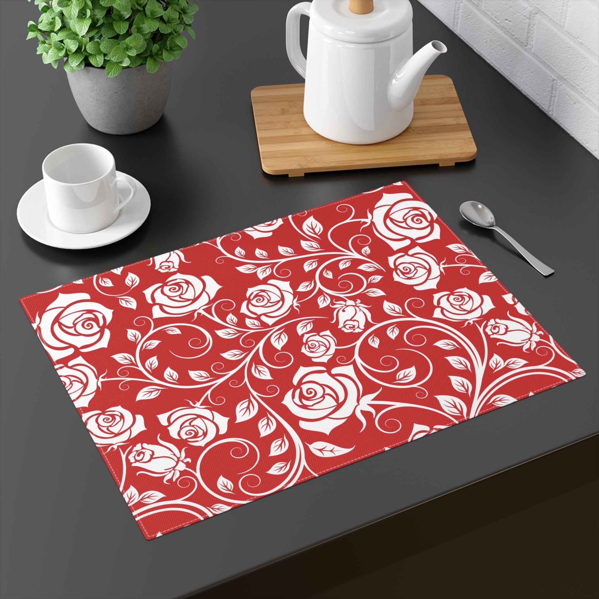Red placemat with white rose pattern on a dark surface with tea set.