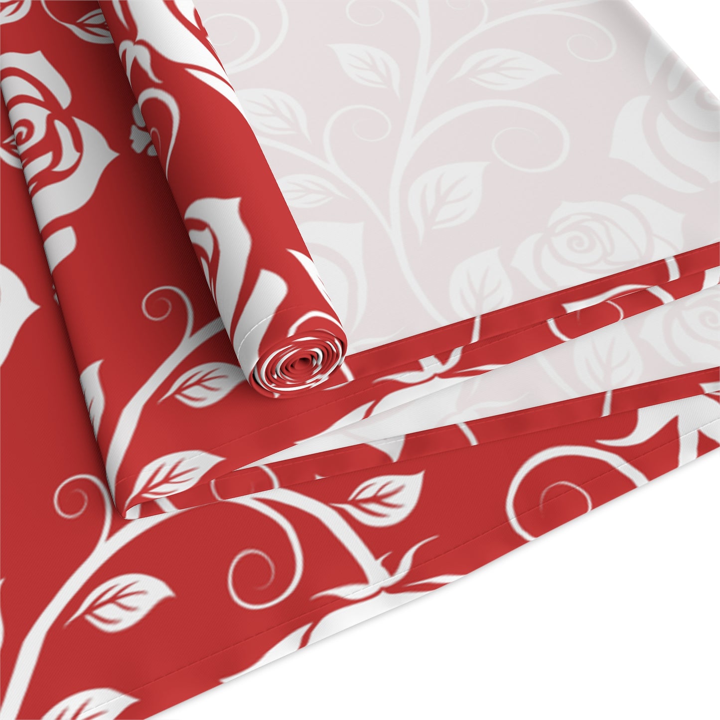 Red and white floral patterned polyester table runner with red and white floral pattern, rolled up and folded on a white background.