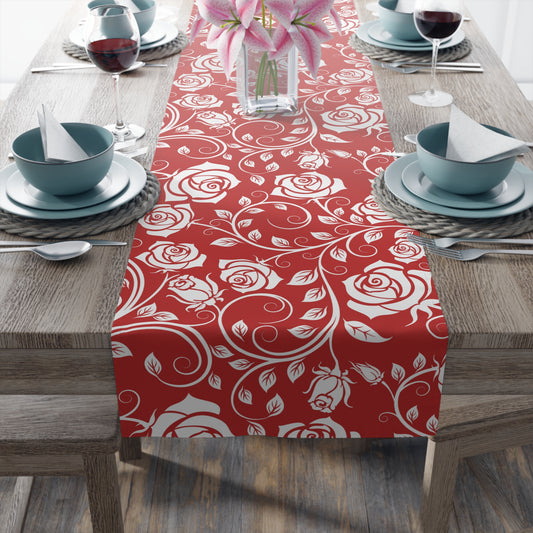 Table setting with a red and white floral polyester table runner on a wooden table.